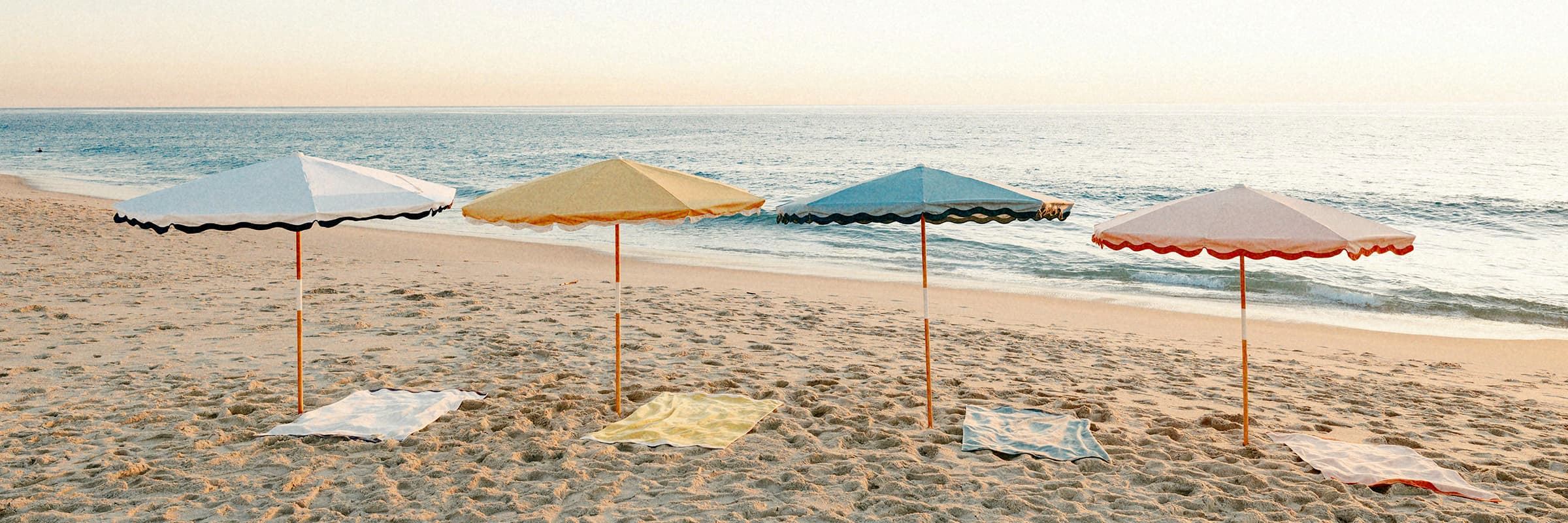 four colorful beach umbrellas on the sand with beach towels under them