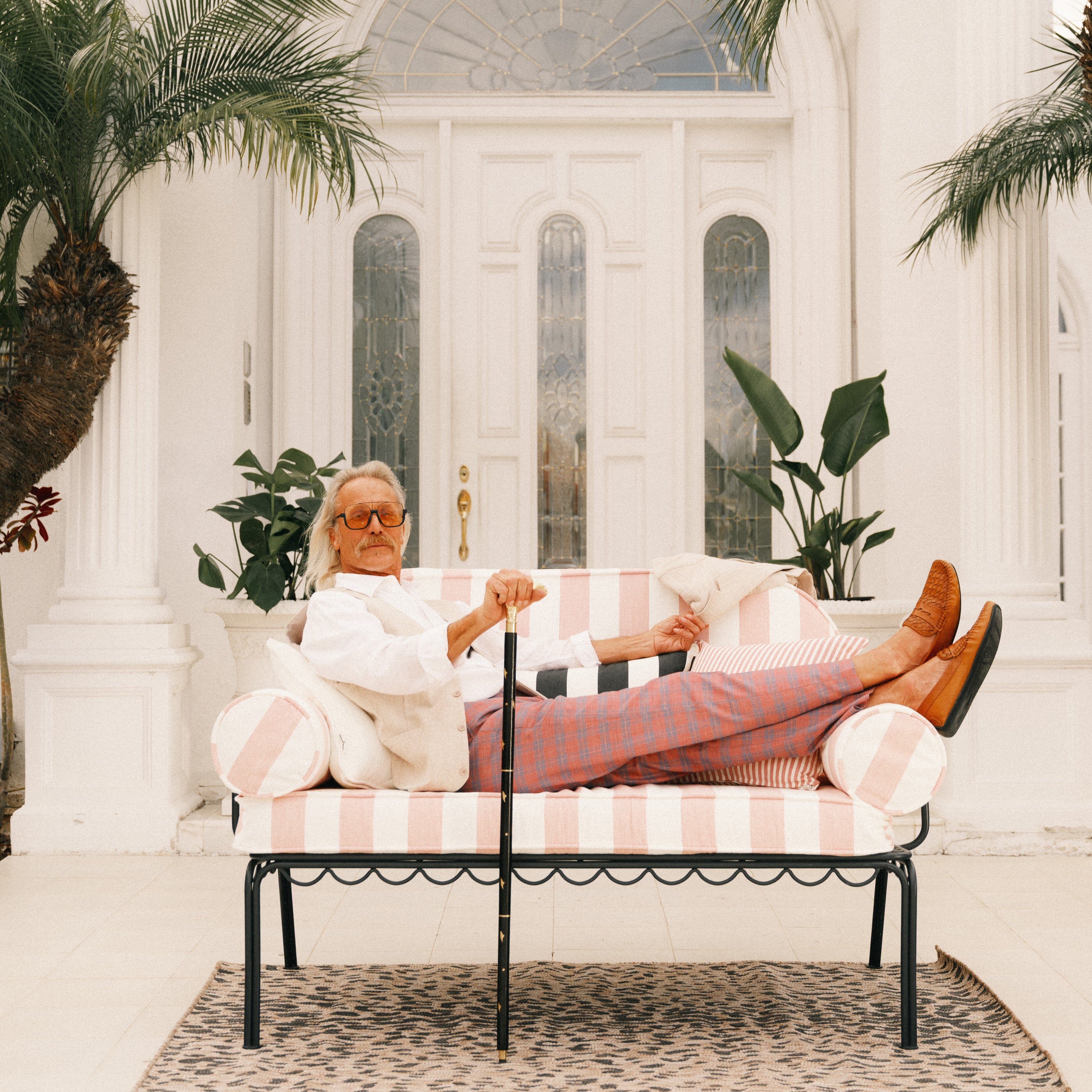 Man sitting on a striped sofa in a bright, sunlit room with plants.