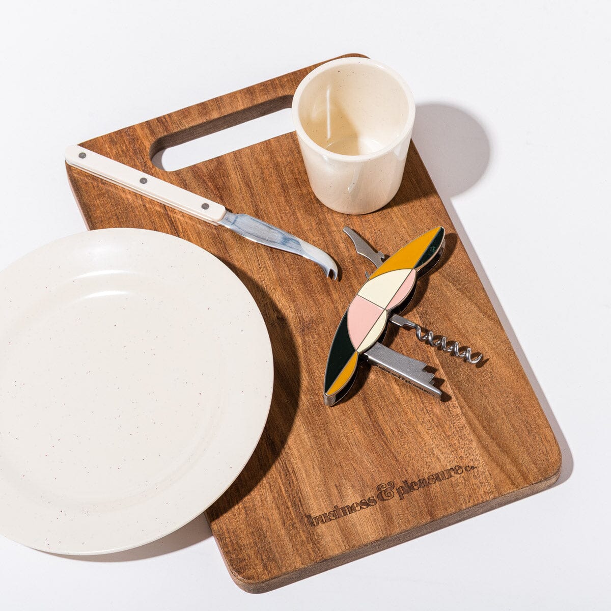 Wooden cutting board with a knife, plate, and corkscrew on a white background