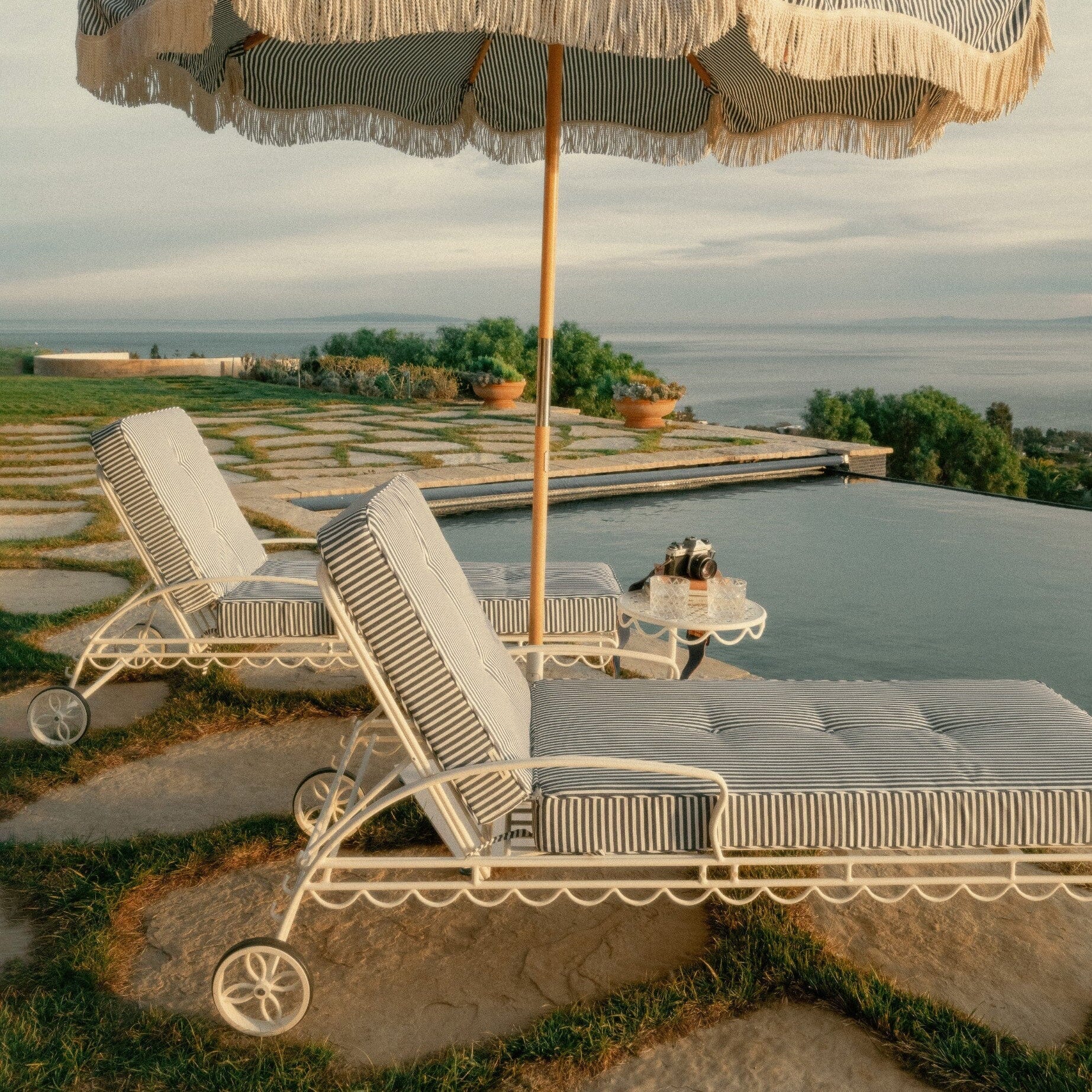 Large decorative umbrella with striped canopy over lounge chairs by a scenic outdoor setting.