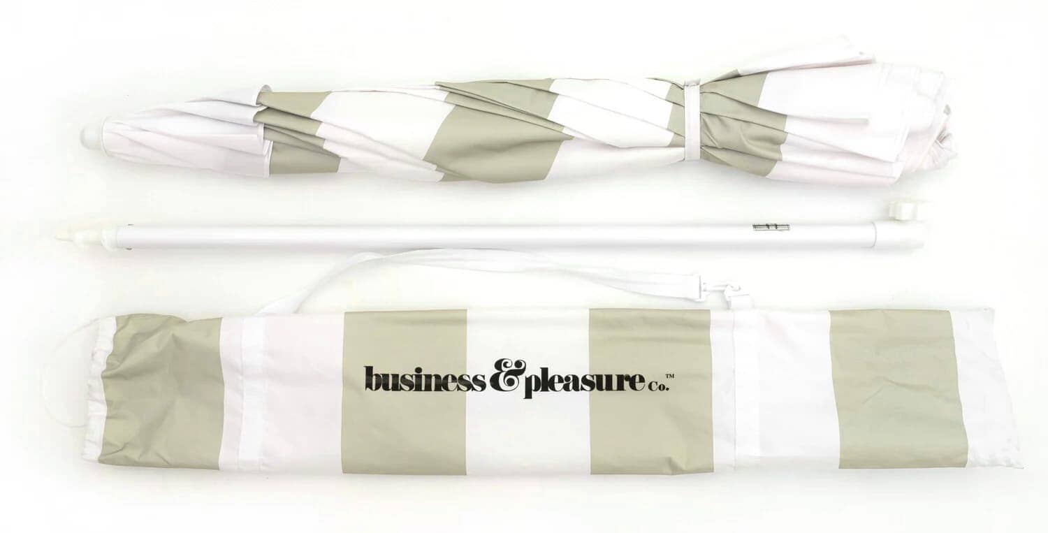 Sage striped umbrella folded up next to the carry case in studio