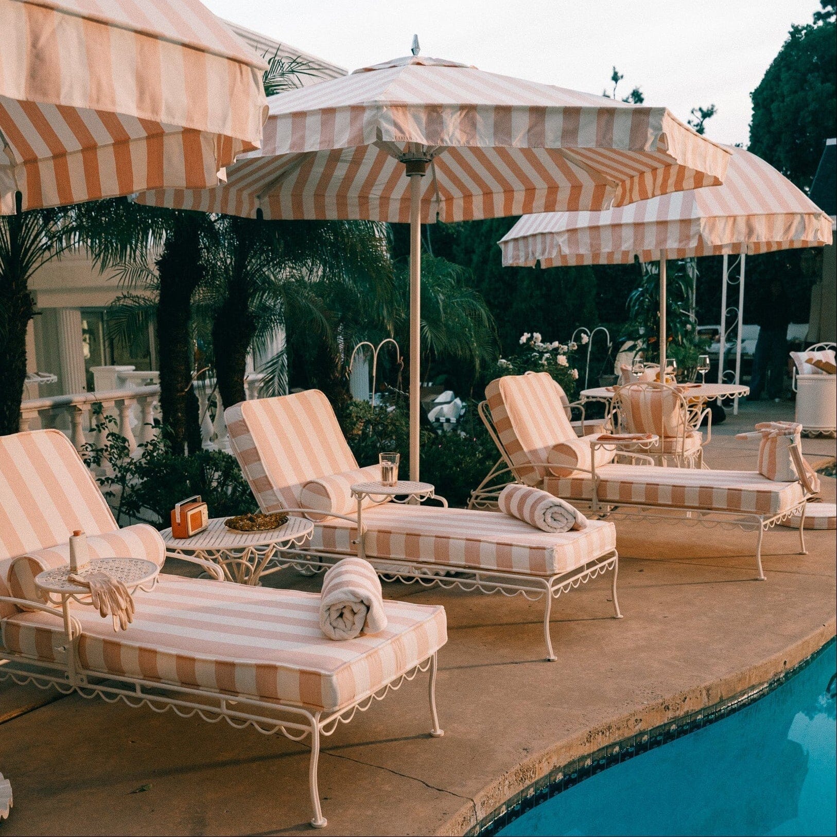 Product image of Poolside area with lounge chairs, striped umbrellas, and a pool.