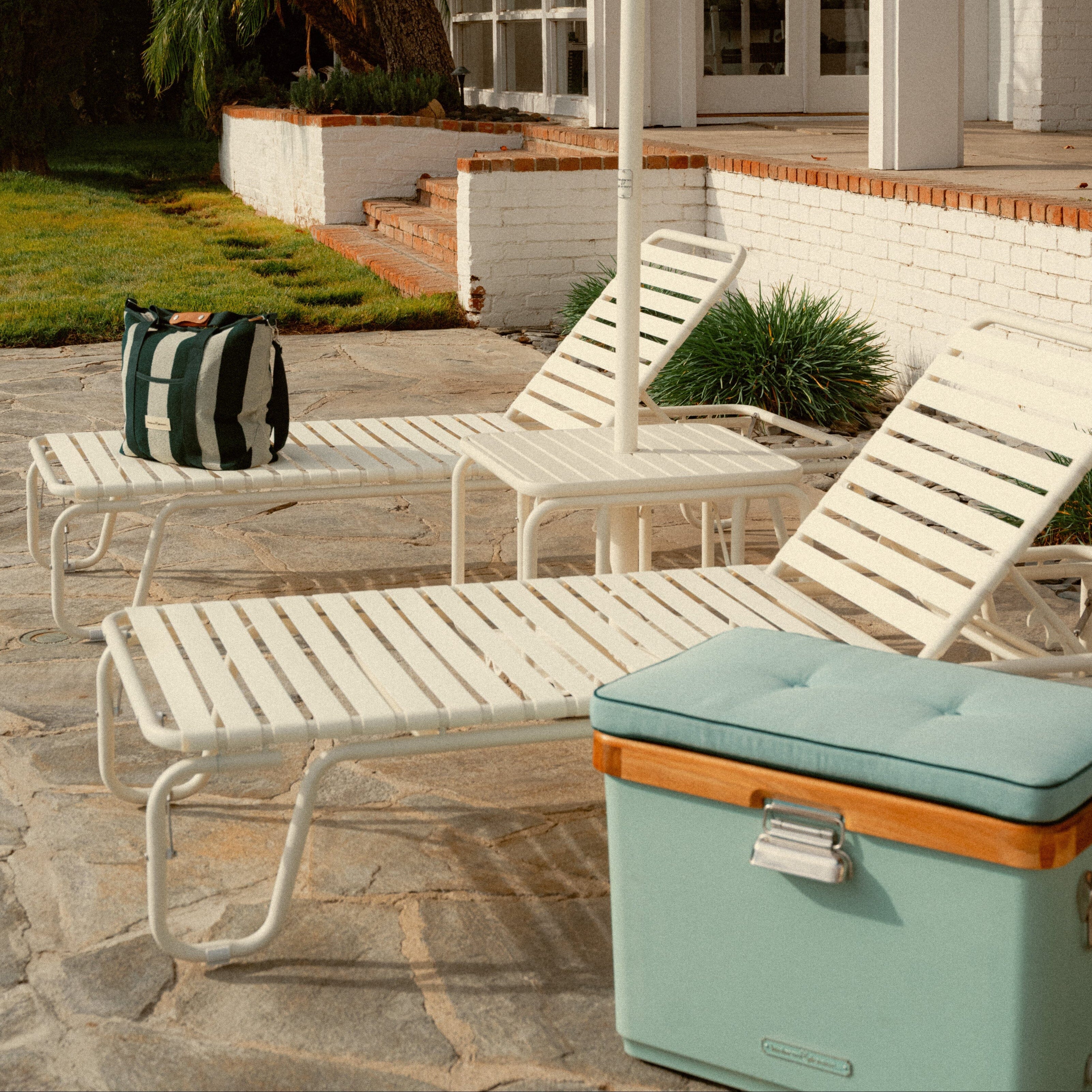 Outdoor patio scene with lounge chairs and a round teal mirror.