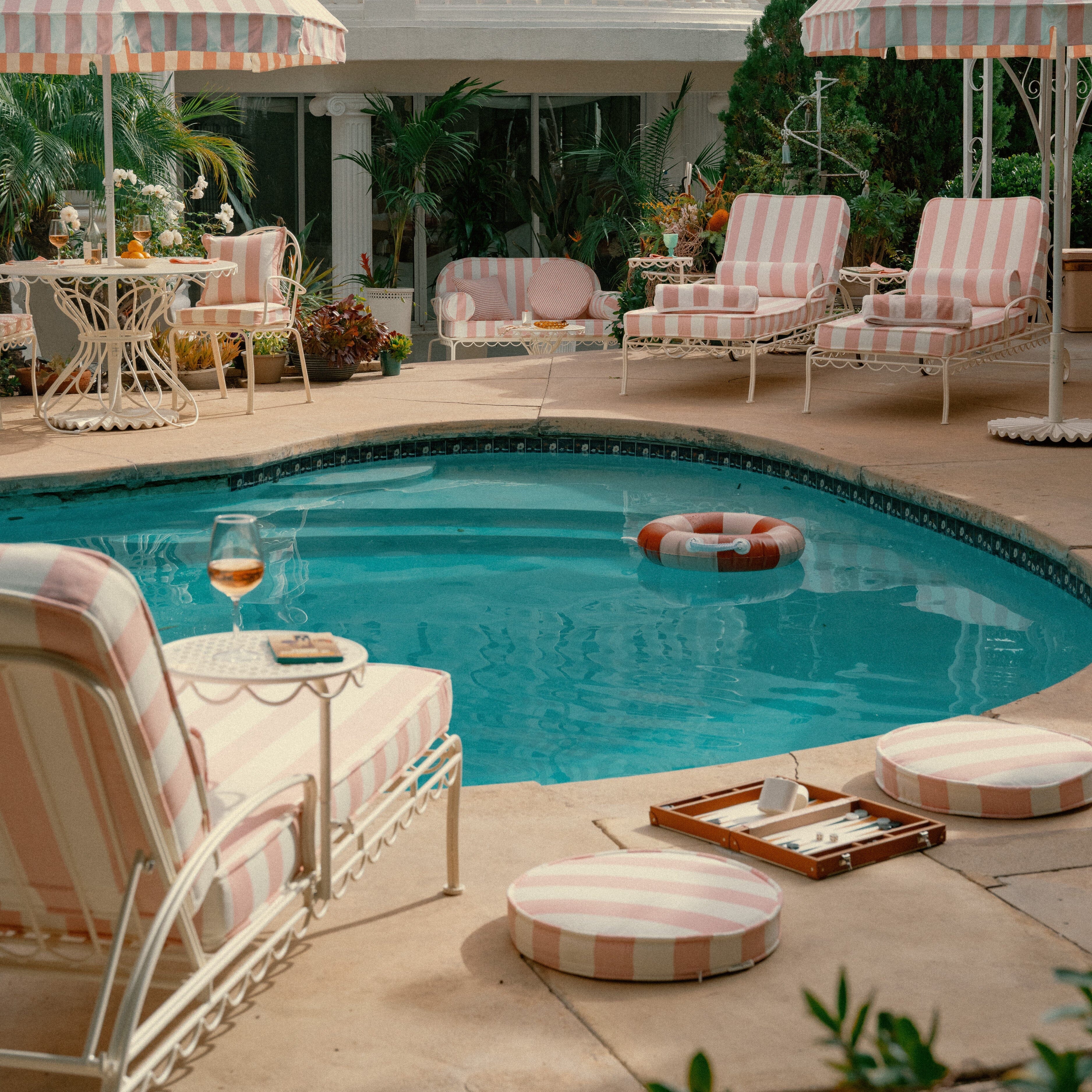Poolside area with striped chairs, umbrellas, and a pool with a life buoy.