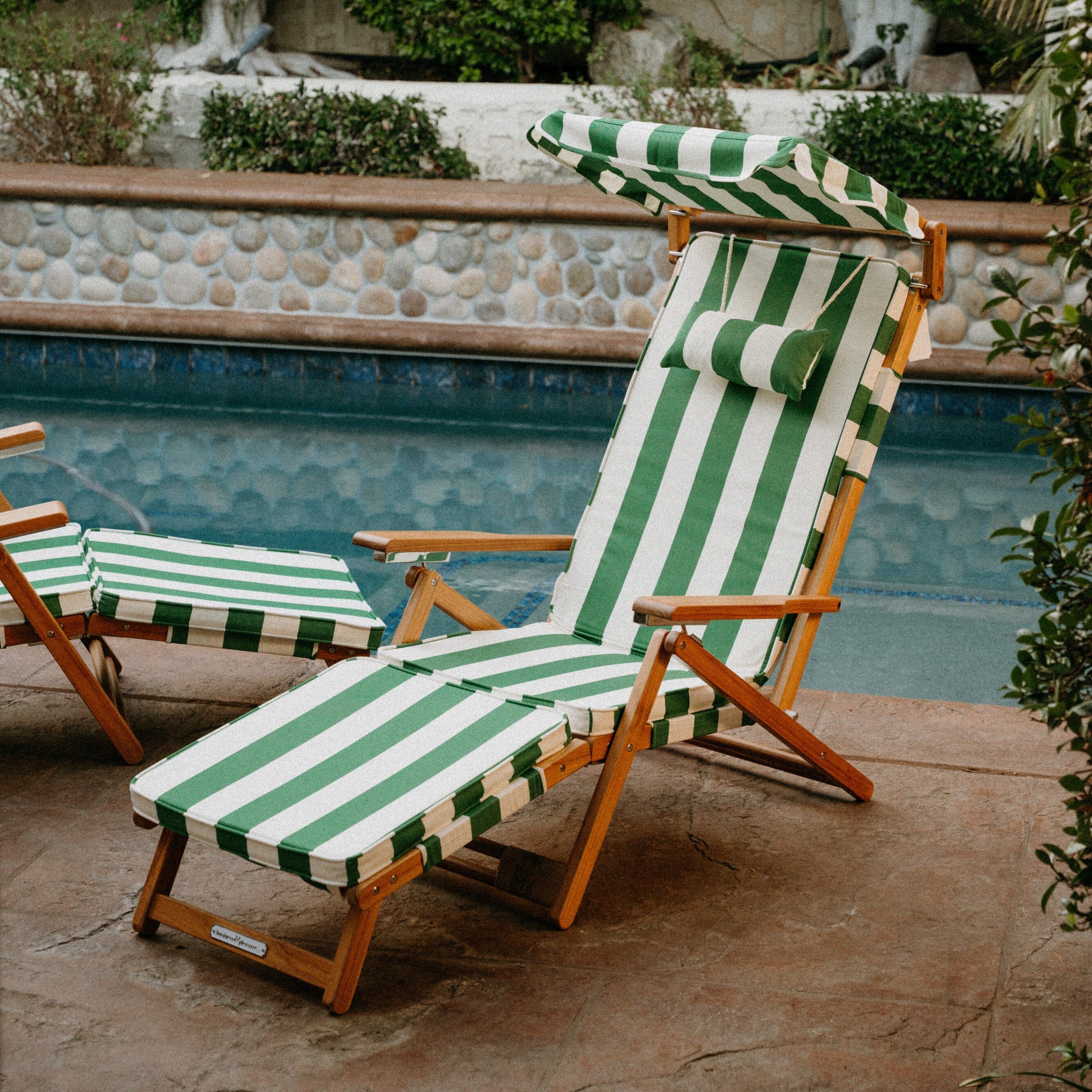 Green and white striped lounge chairs by a poolside with a garden background