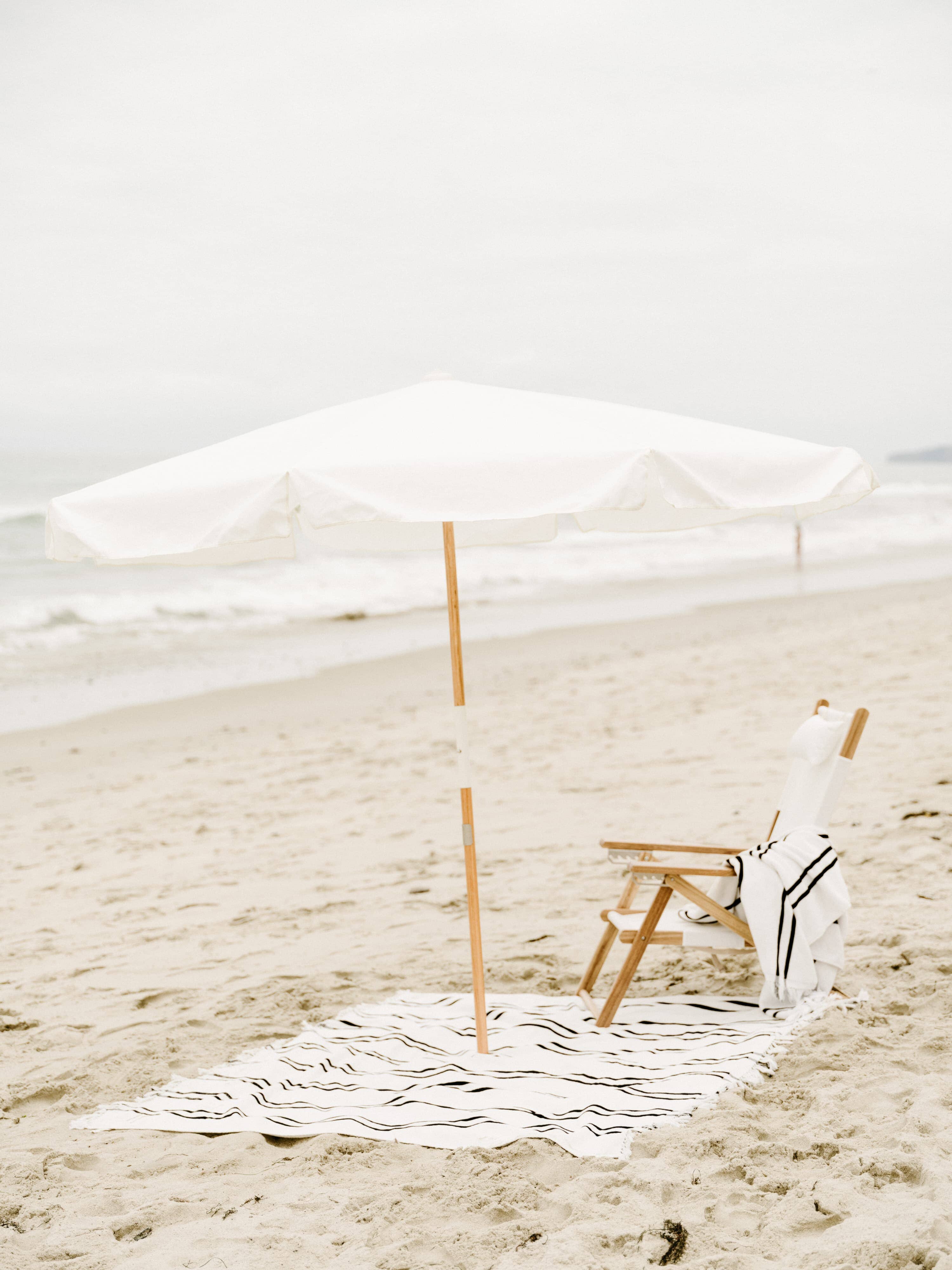 white amalfi umbrella at the beach with chair and blanket