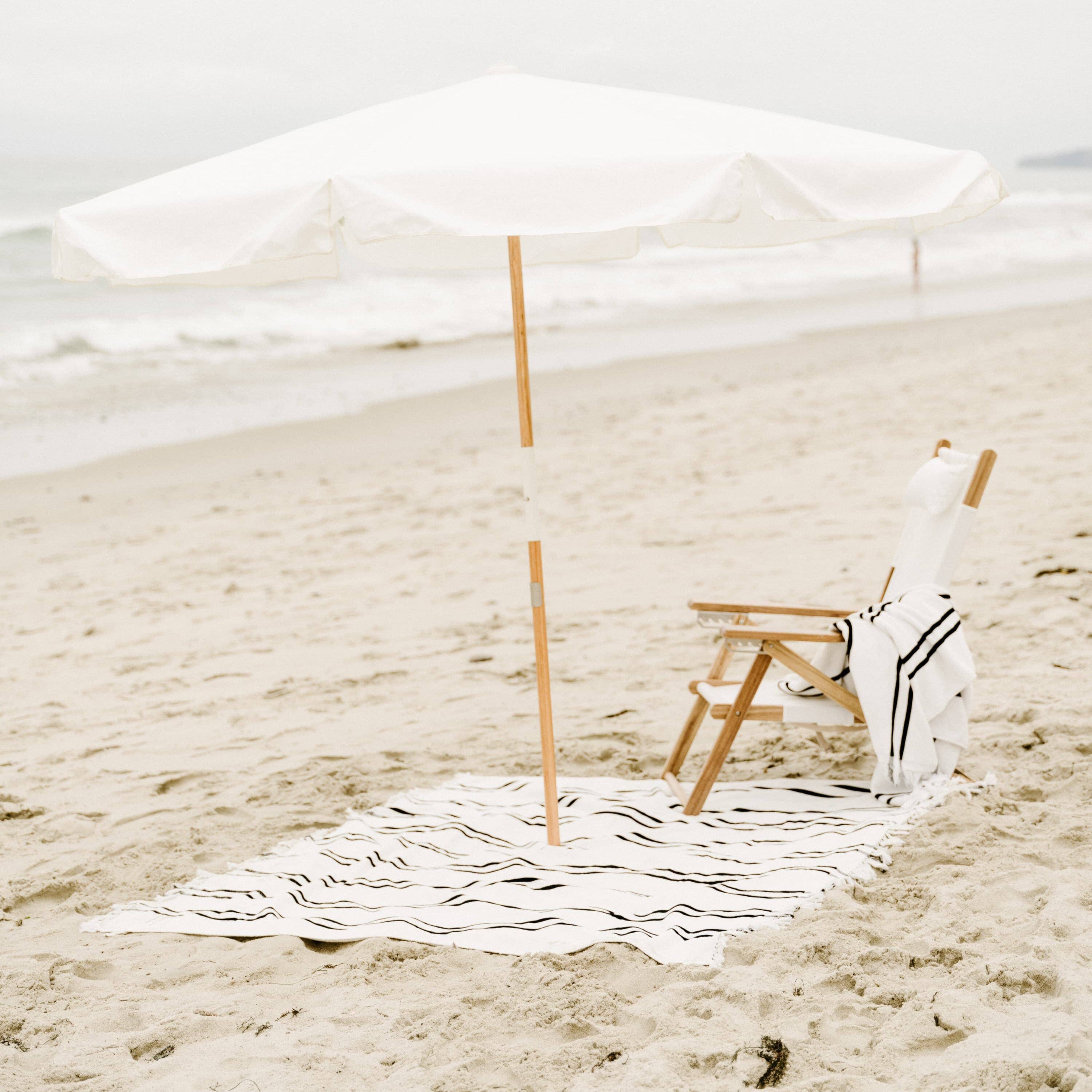 white amalfi umbrella at the beach with chair and blanket