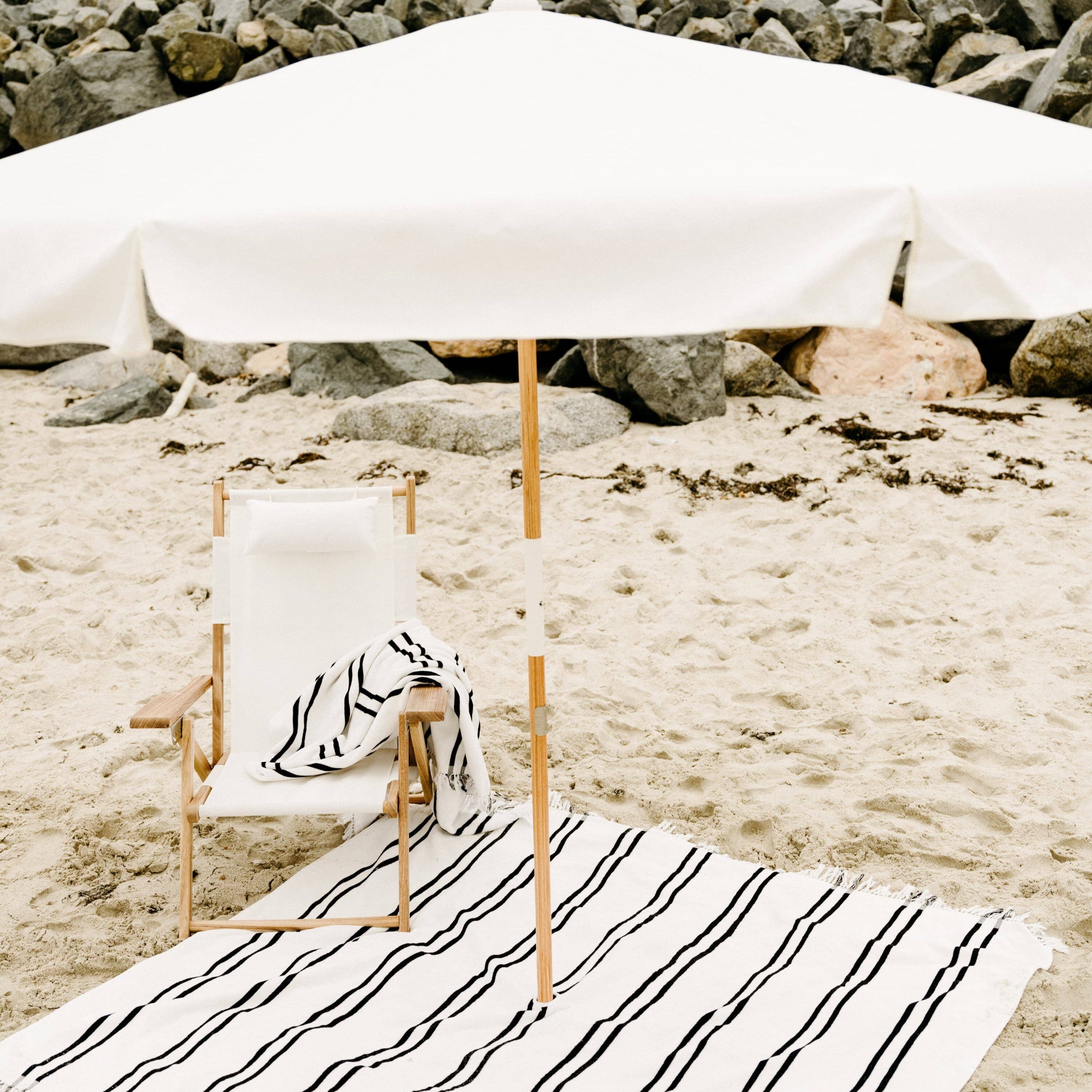 white amalfi umbrella at the beach with chair and blanket