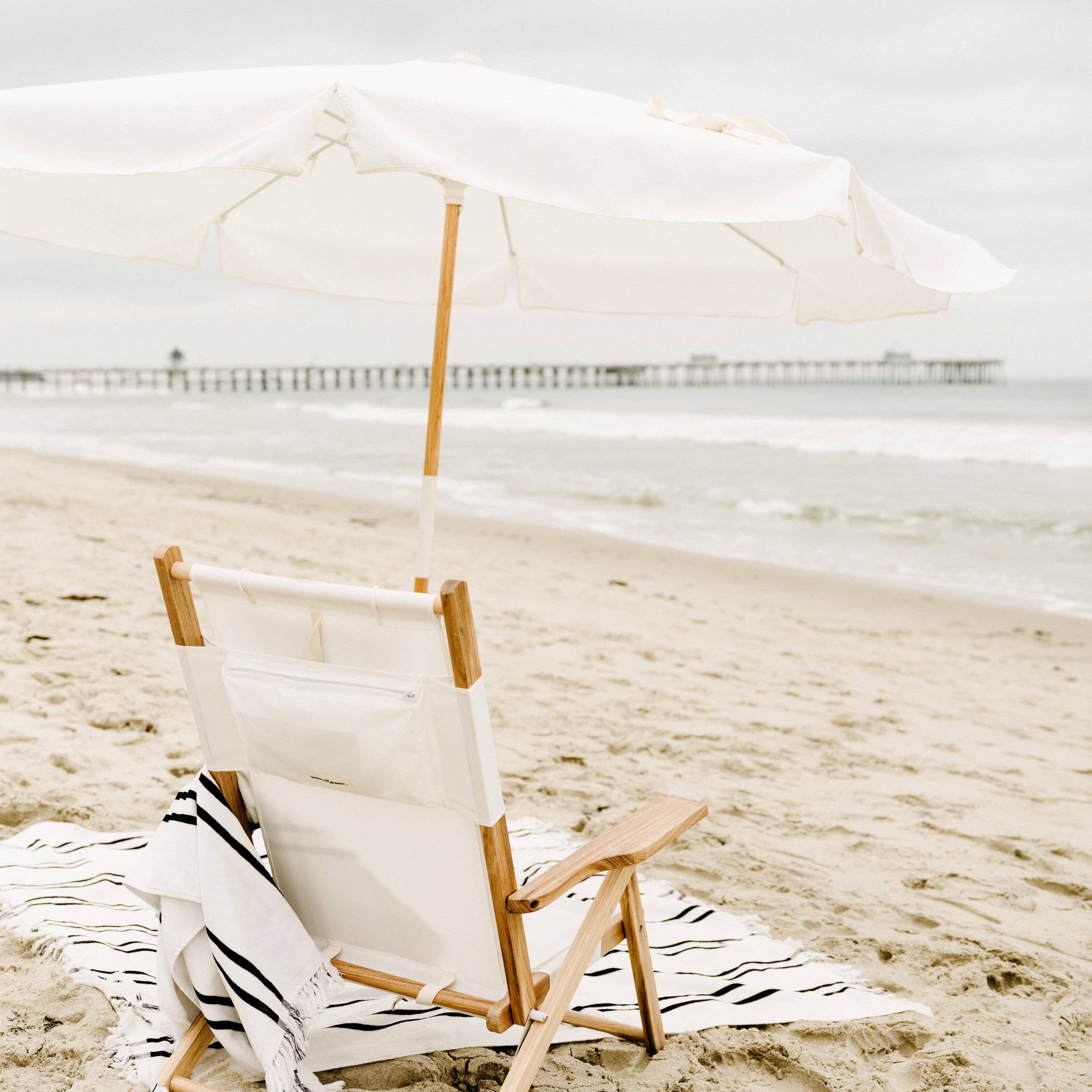 white amalfi umbrella at the beach with chair and blanket