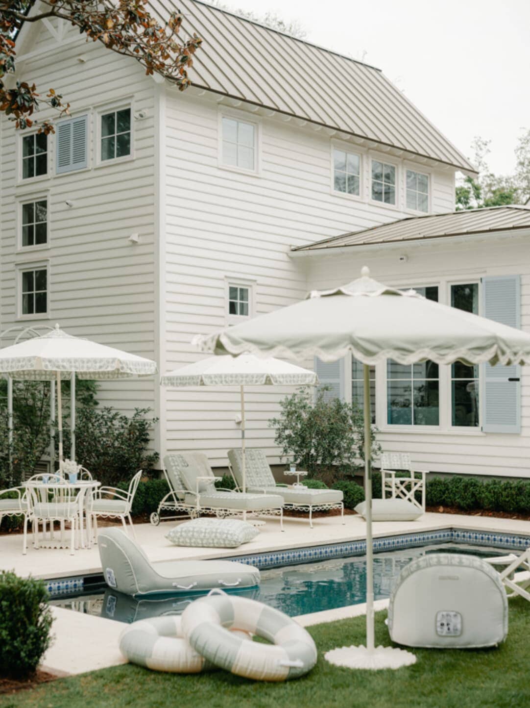 Backyard pool area with umbrellas, tables, lounges and pool floats