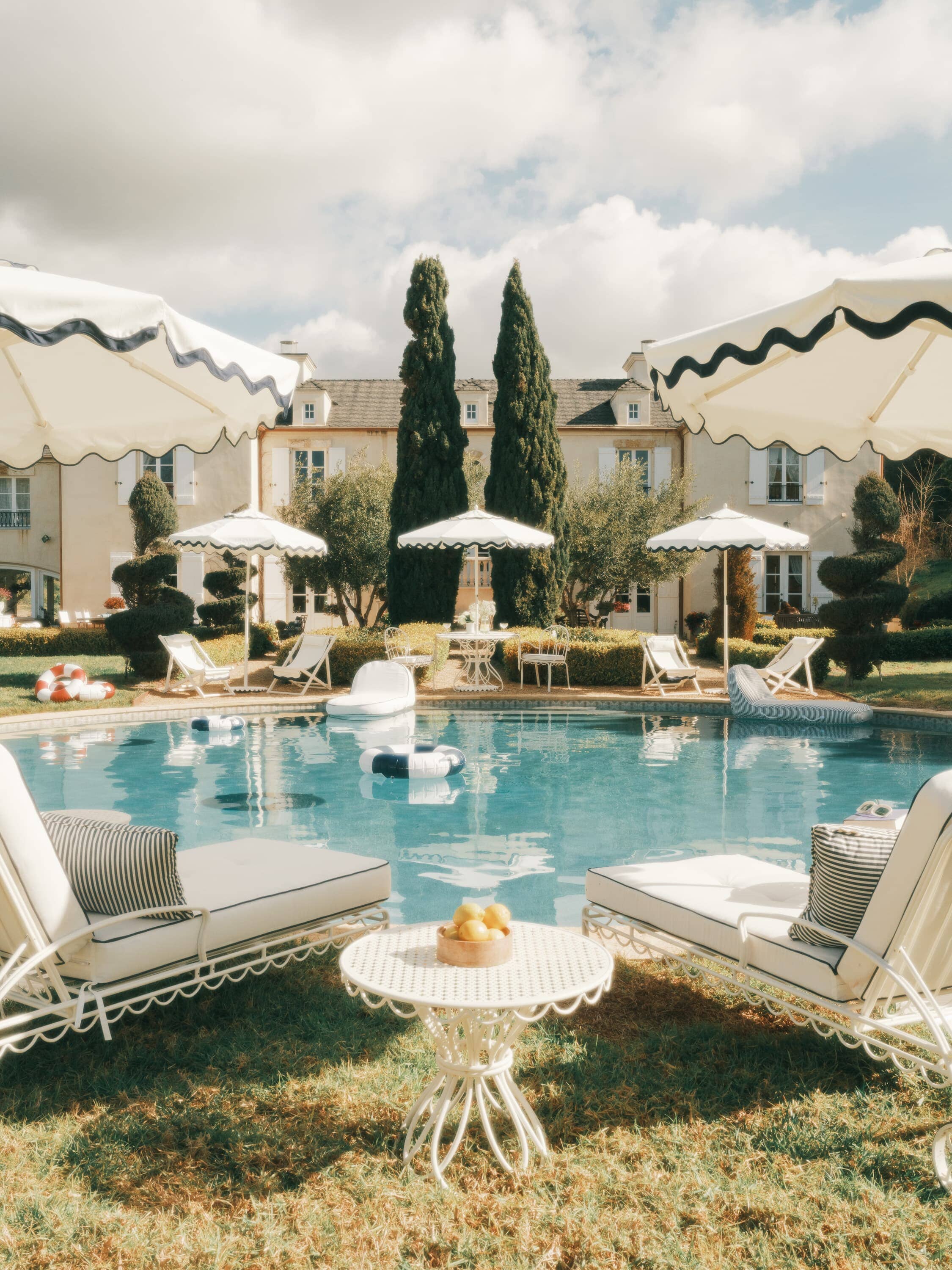 White riviera market umbrellas with sun loungers next to a pool