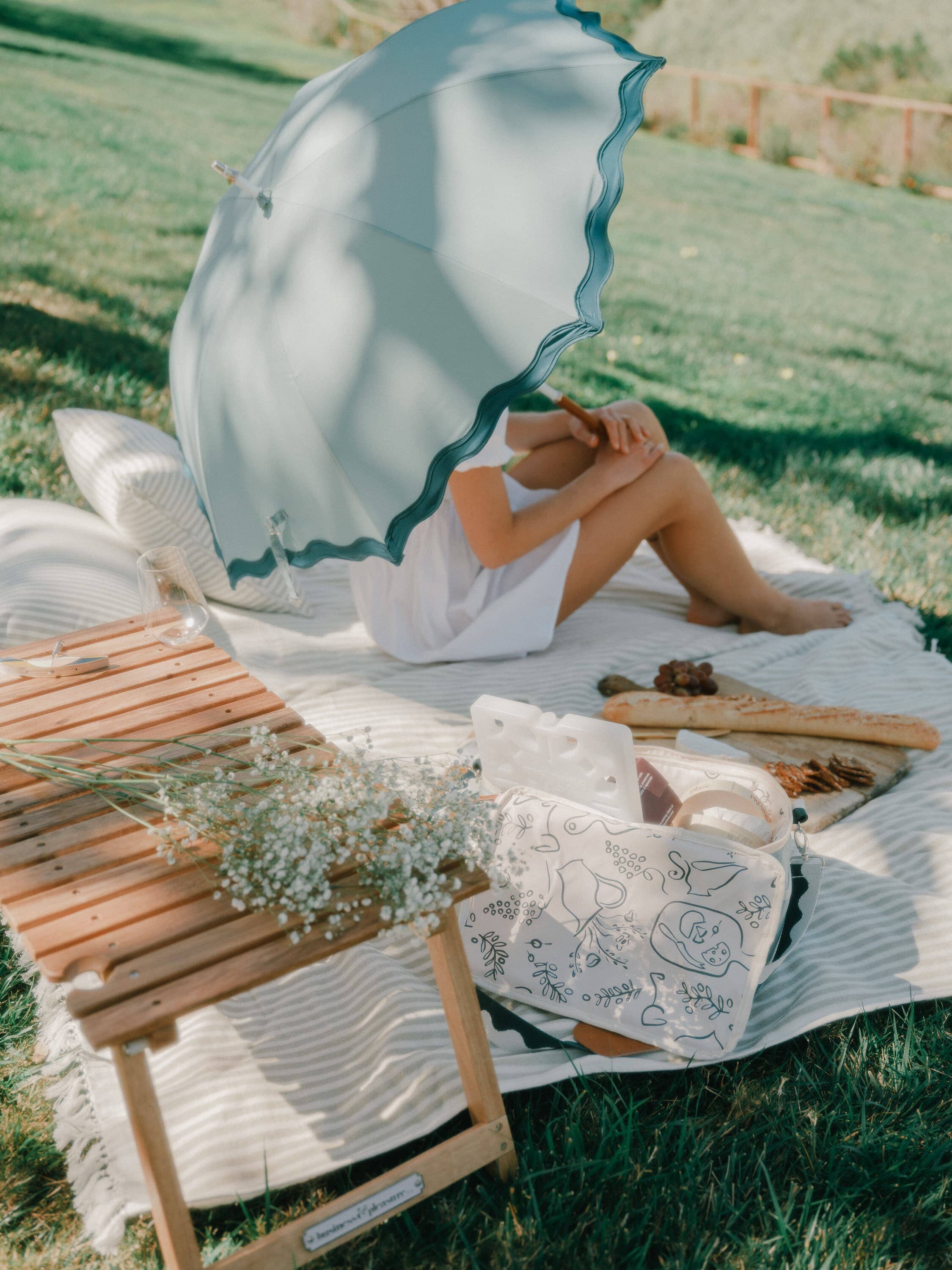 outdoor picnic with riviera green rain umbrella, sage blanket, folding table and cooler bag