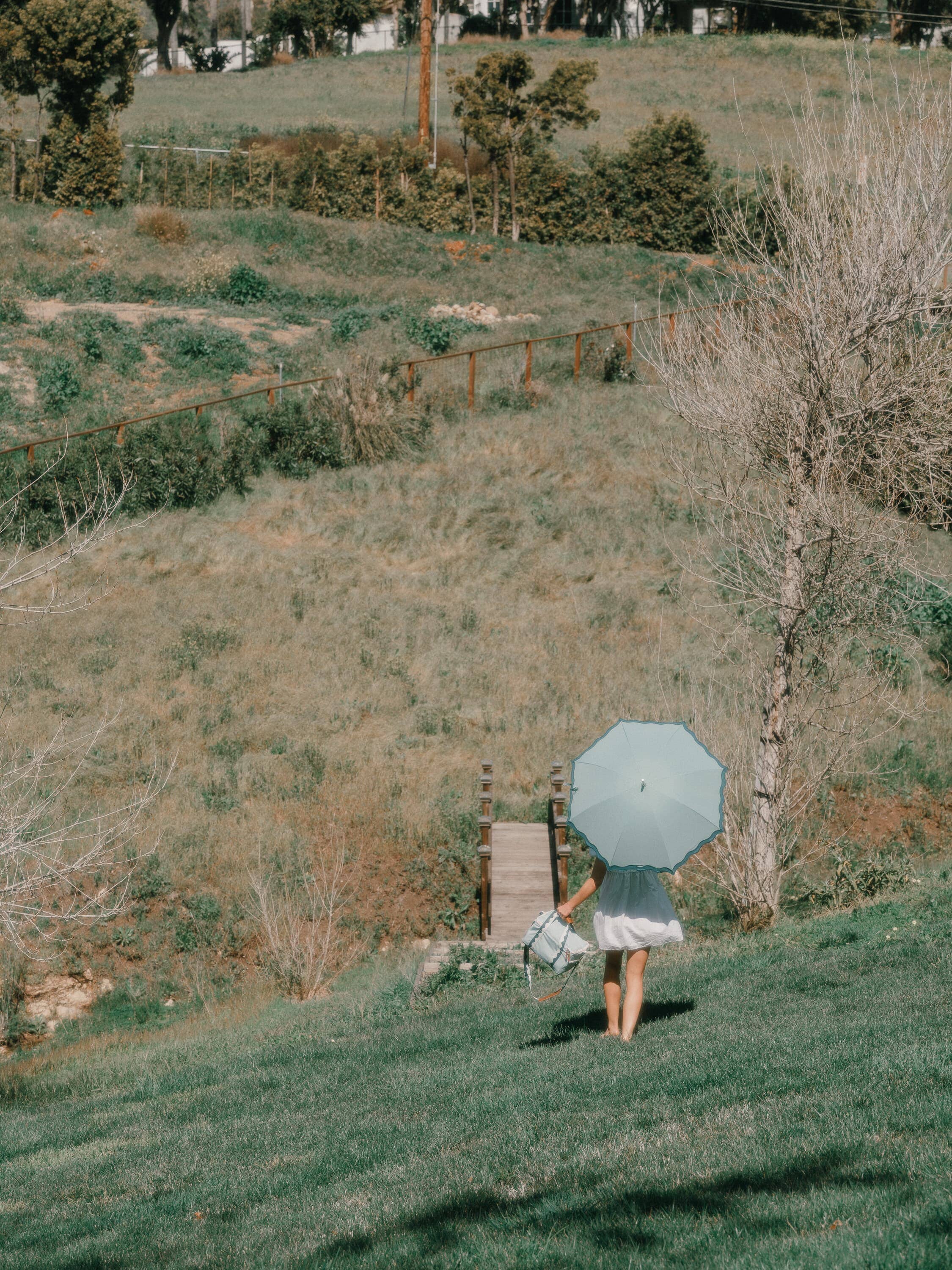 Riviera green rain umbrella shading a lady in a grass field.