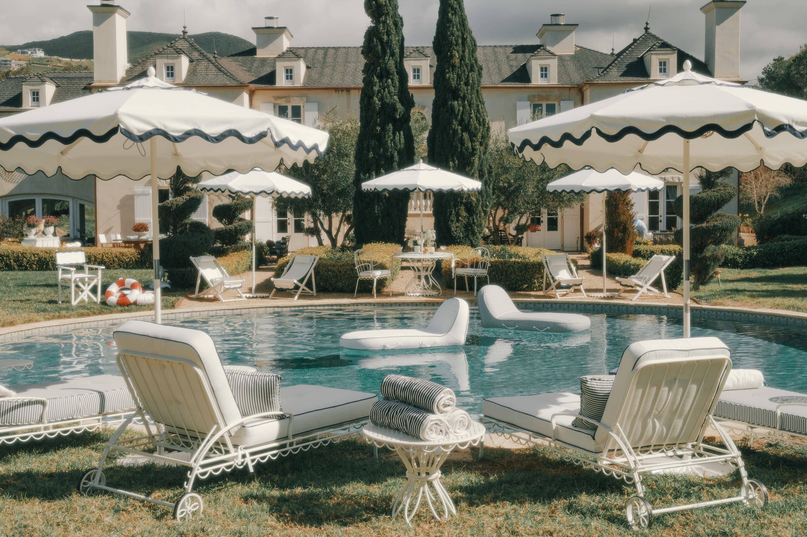 Backyard pool setting with tables, chairs, umbrellas and sun loungers