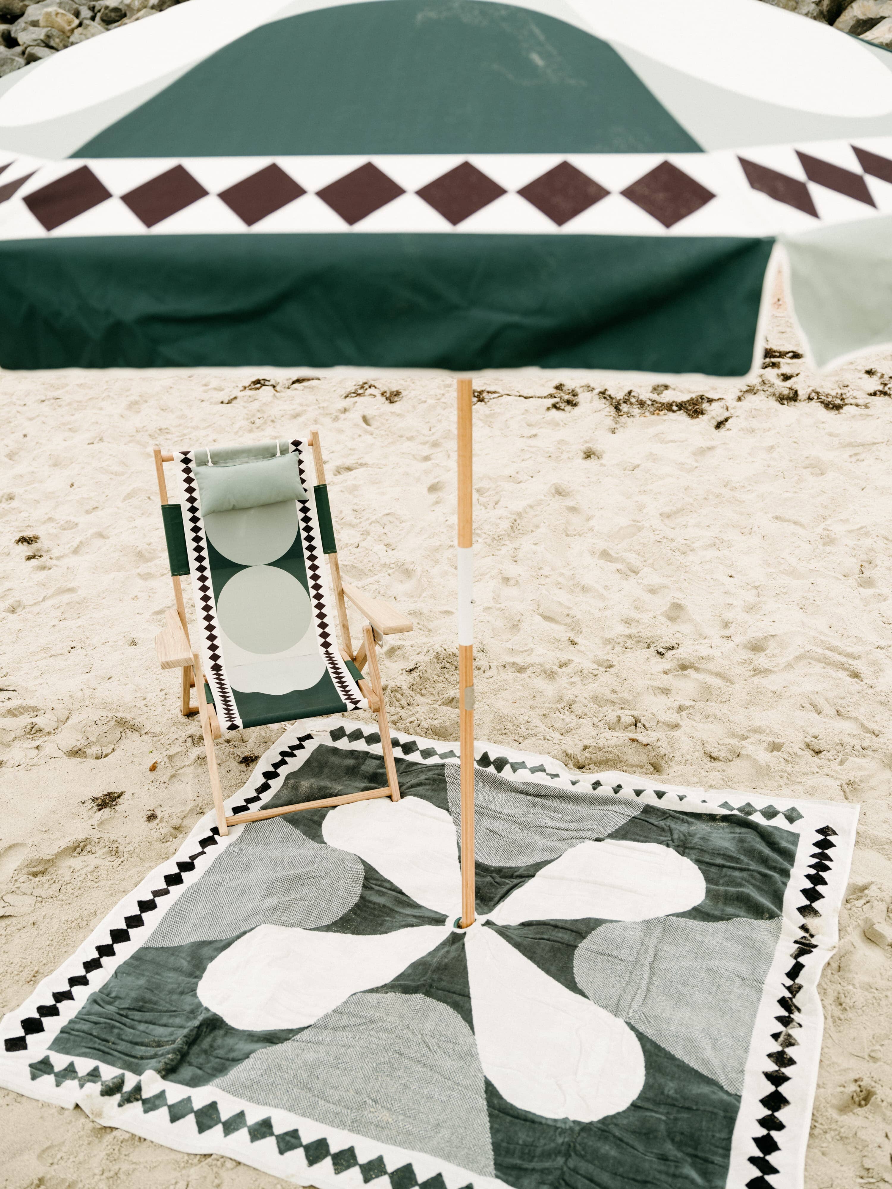 Beach set up with diamond green umbrella, chair and blanket.