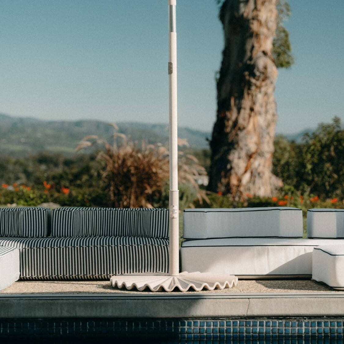 white clamshell base next to a pool with an umbrella and cushions