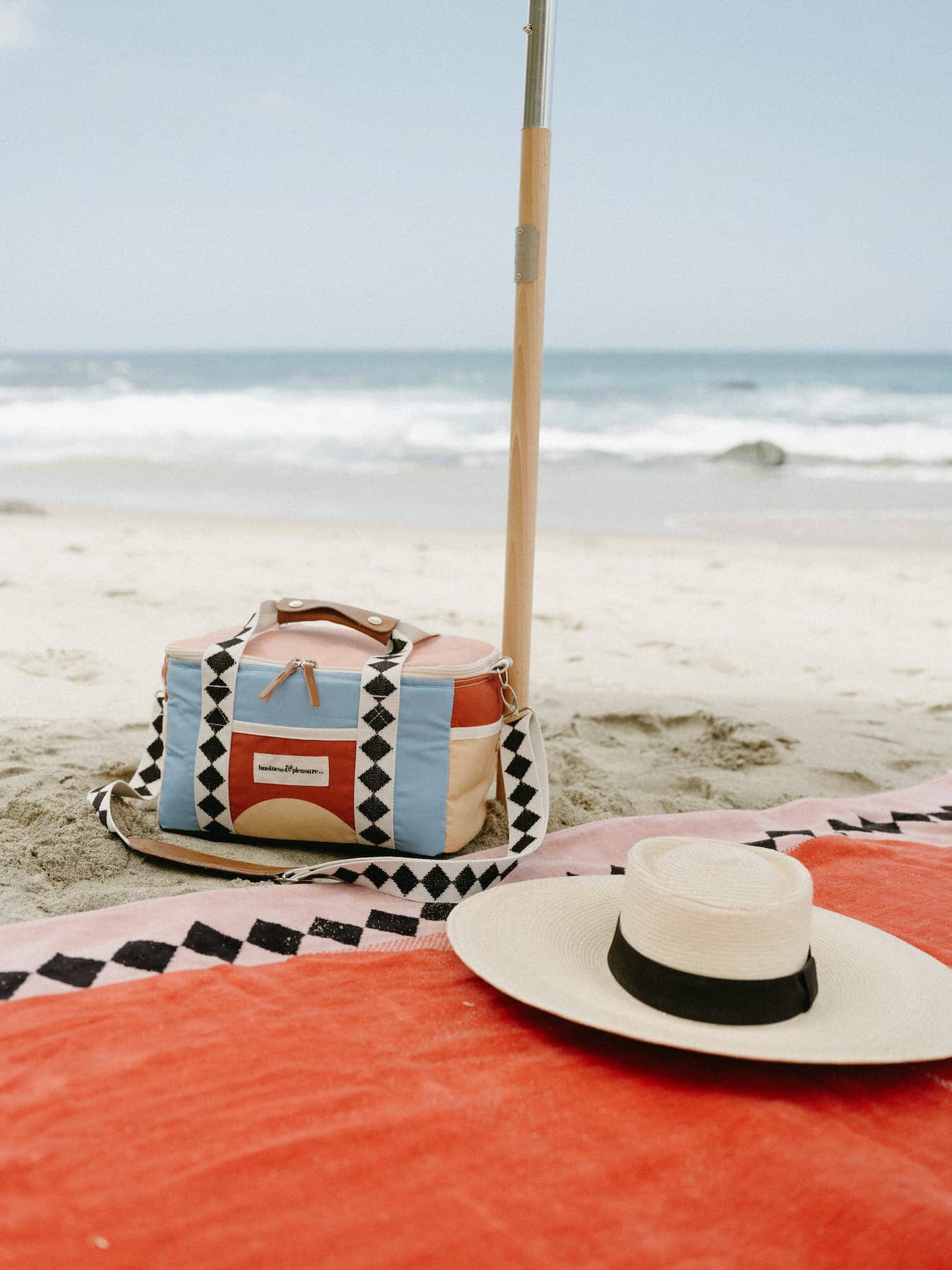 Diamond pink towel and cooler on the beach with a hat