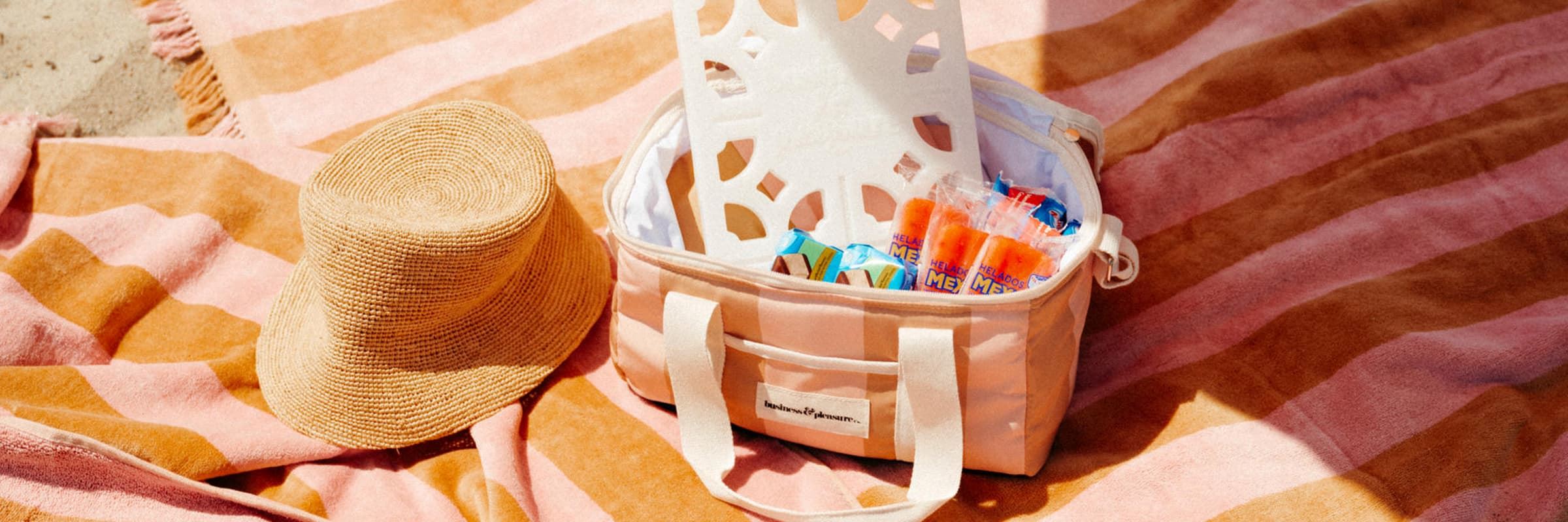pink and gold striped cooler with a hat and towel on the beach