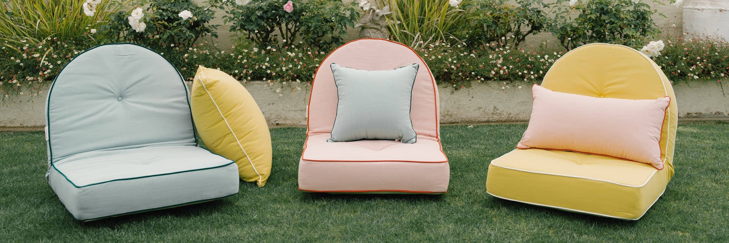 three colorful reclining pillow loungers with outdoor throw pillows on a lawn
