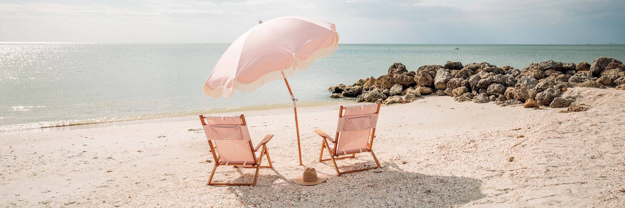 pink striped beach umbrella and two chairs on the sand