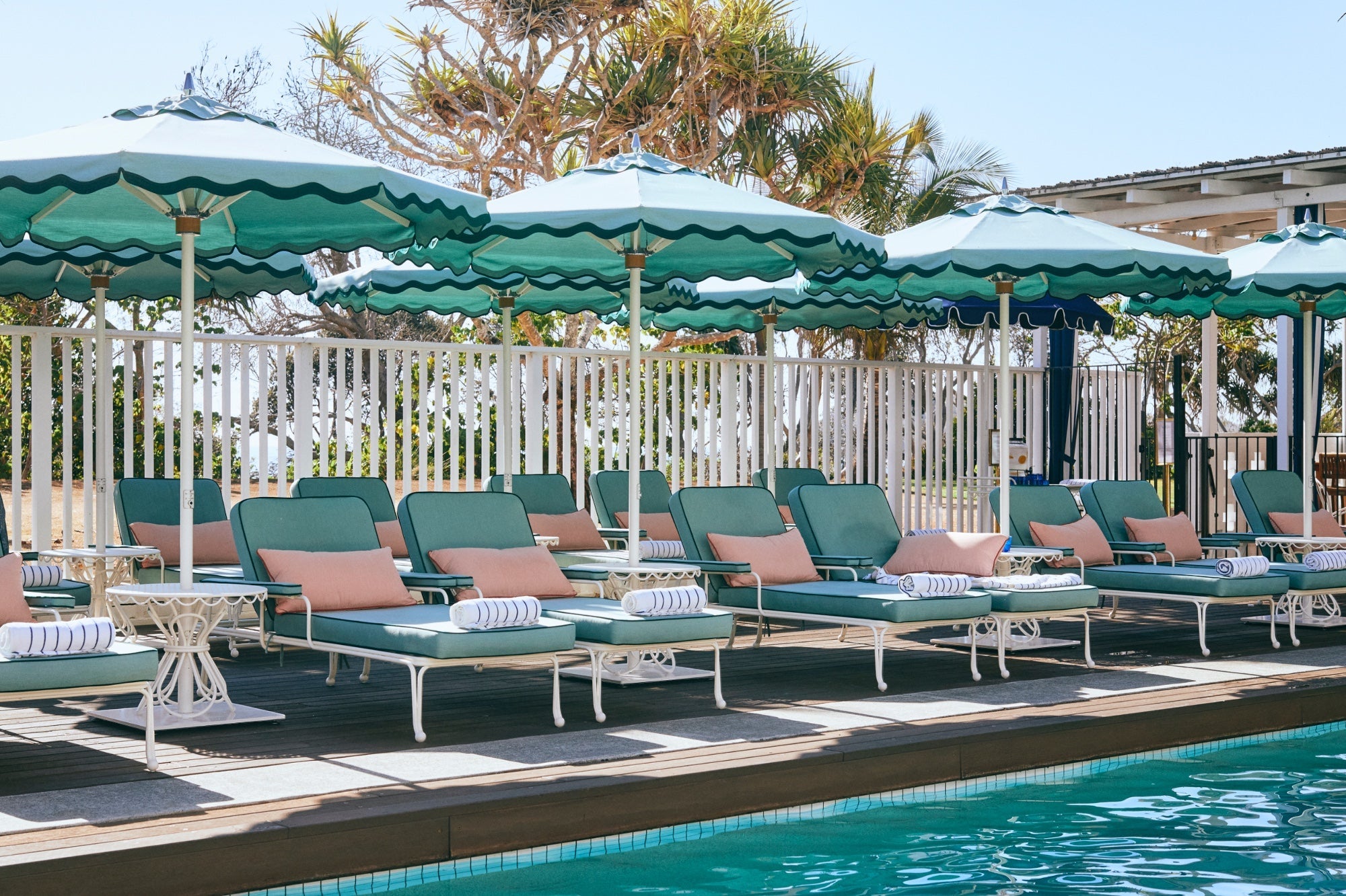 Poolside area with lounge chairs and green umbrellas by a pool.