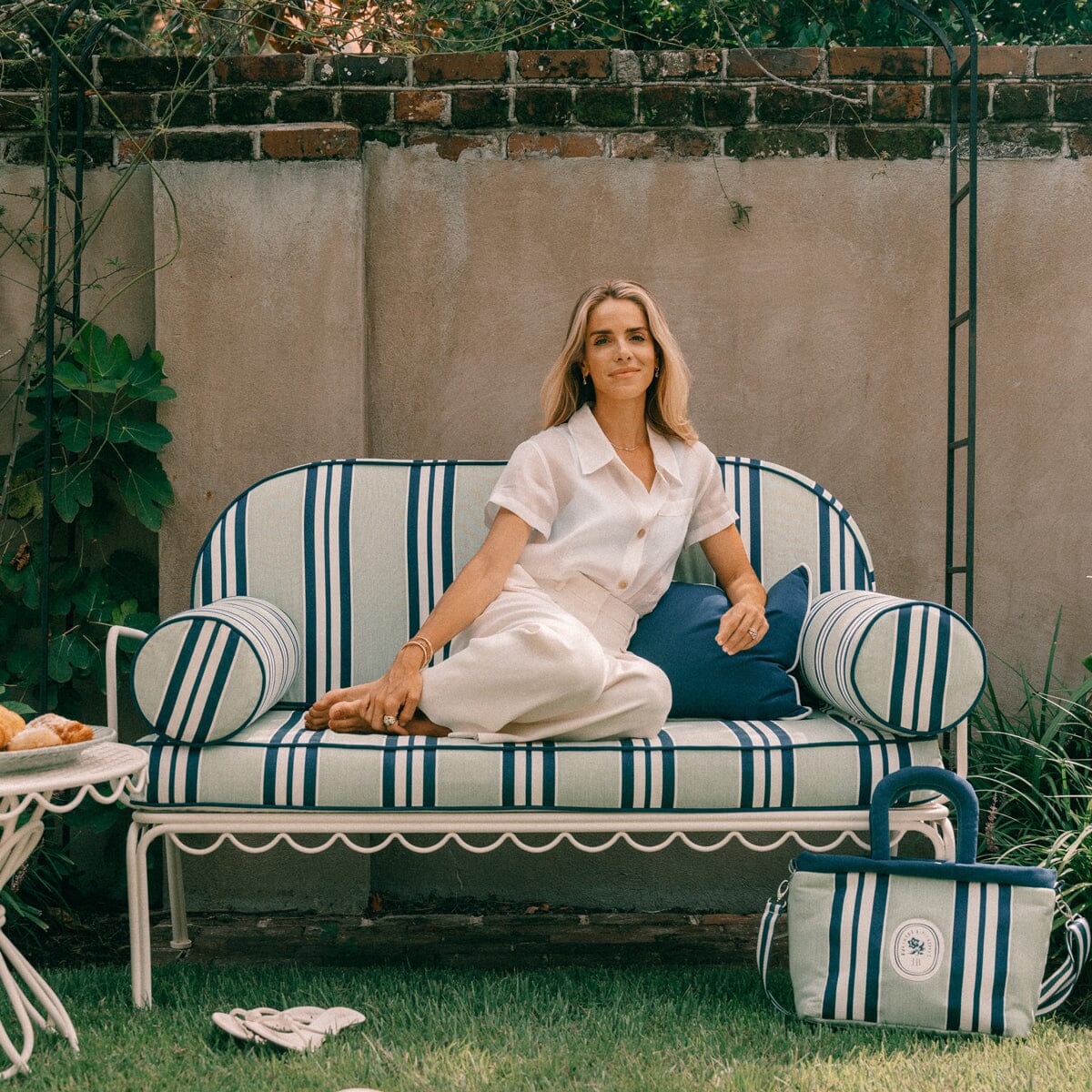 Julia Berolzheimer sitting on the Al Fresco Love Seat in Antique White and her signature Green Stripes Cushion Slip Cover.