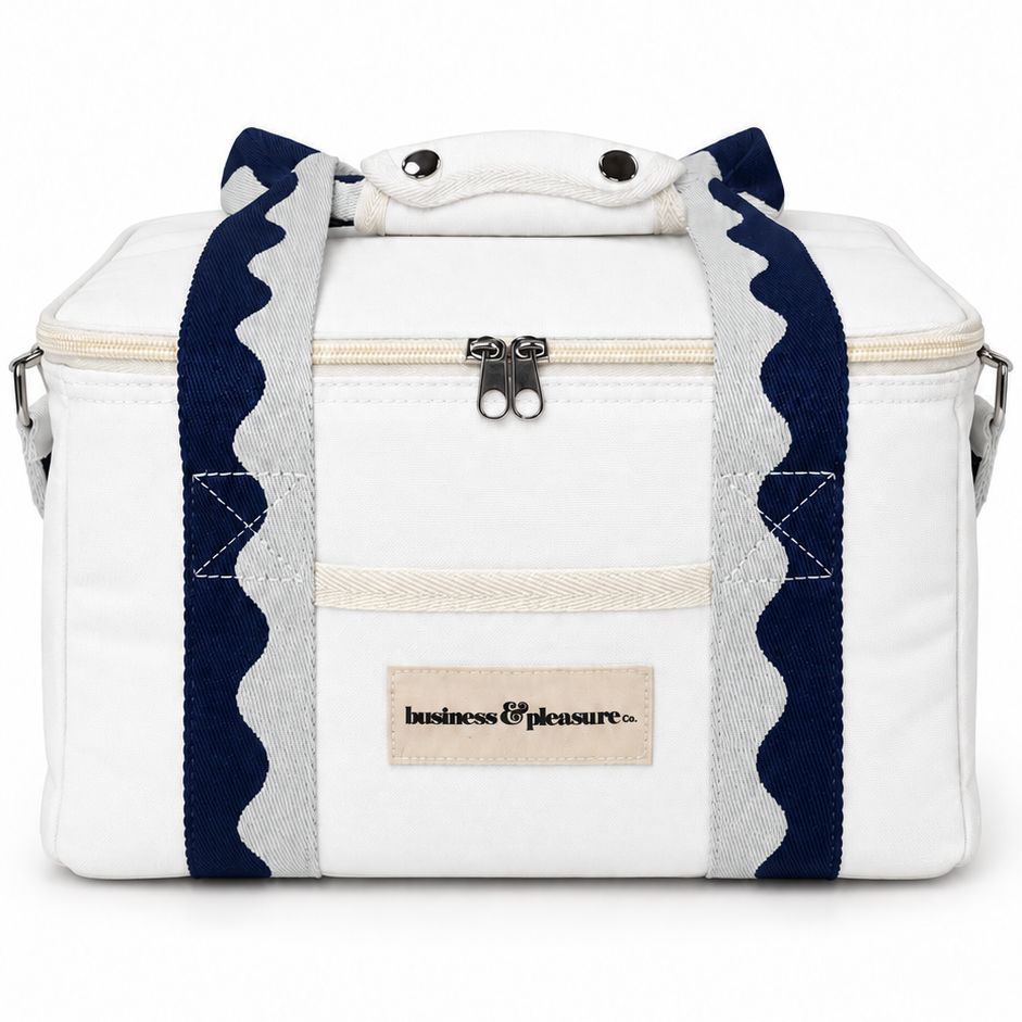 A white soft-sided cooler bag with navy blue and white scalloped handles, a top zipper, and a beige brand patch reading 'business pleasure' on the front.