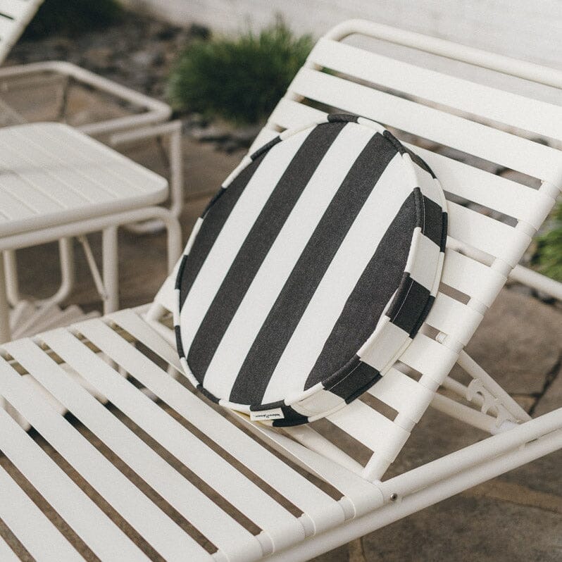 Black and white striped pillow on a white lounge chair outdoors.
