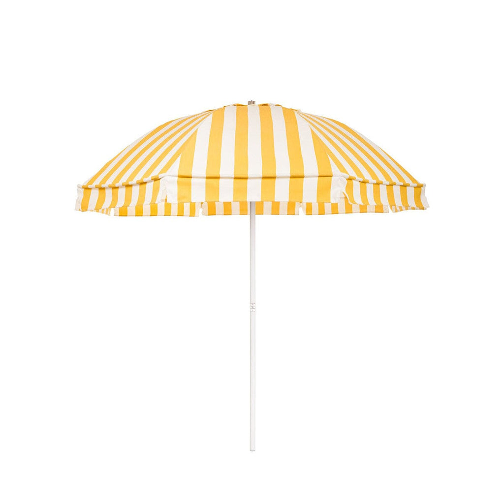 The Patio Umbrella by Business & Pleasure Co. in Crew Mimosa Yellow Stripe features equally spaced yellow and white stripes throughout the umbrella canopy, which is in a dome shape and on a white pole.