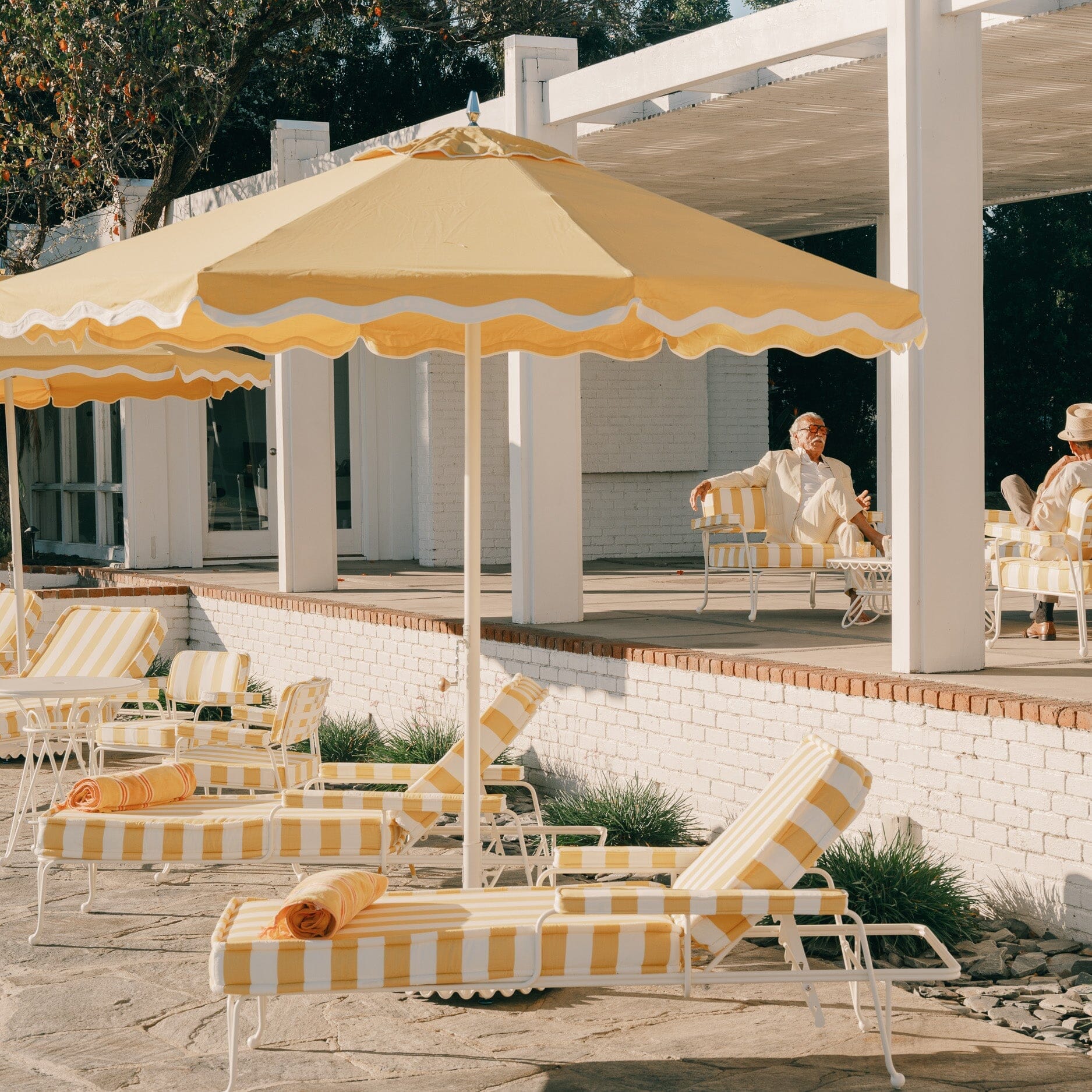 Outdoor patio with yellow and white striped furniture and umbrellas, people sitting and enjoying the area.