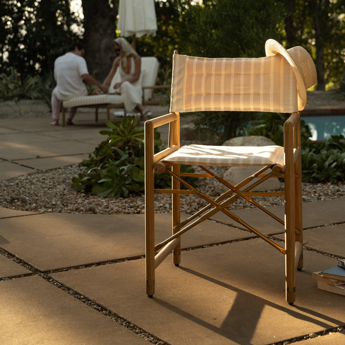 Wooden chair with a woven backrest on a stone patio with people and an umbrella in the background.