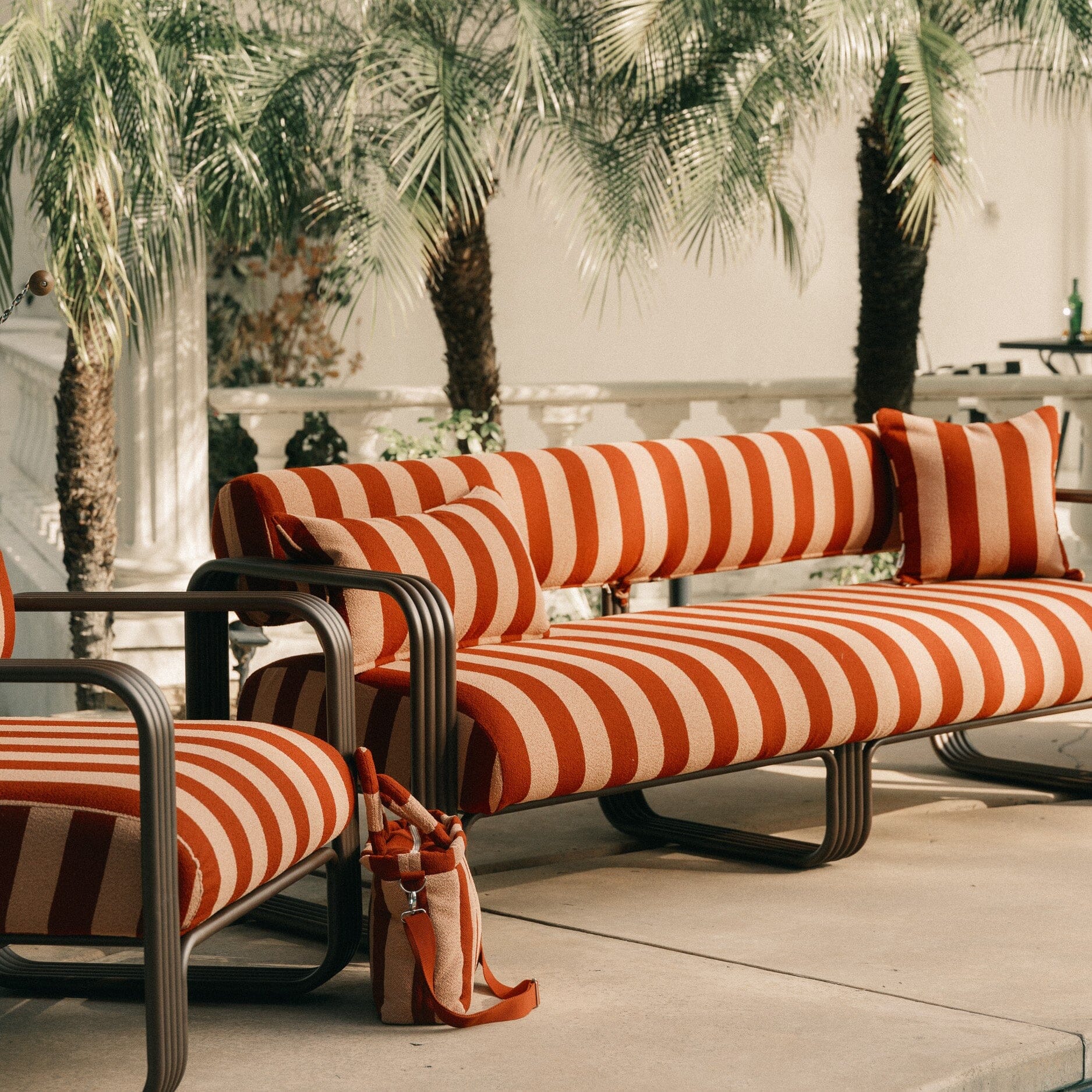 Outdoor furniture with red and white striped cushions and an umbrella, palm trees in the background.