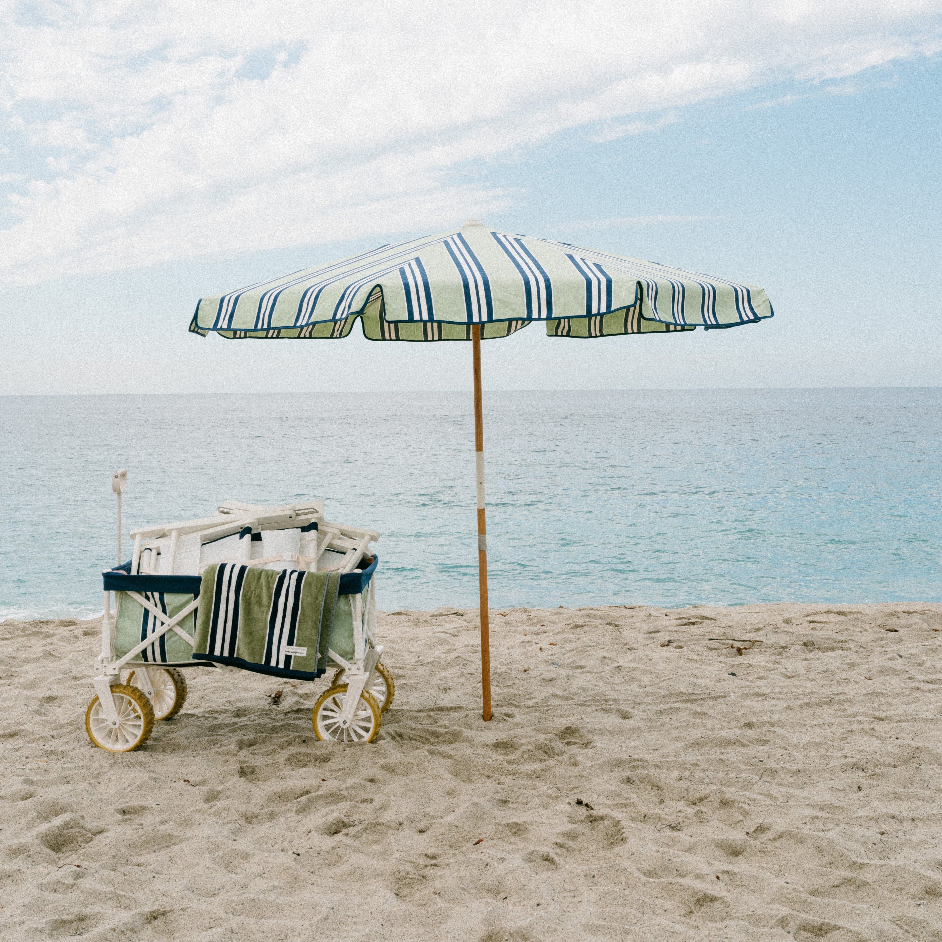 Beach cart under a striped umbrella on a sandy beach with ocean and sky in the background