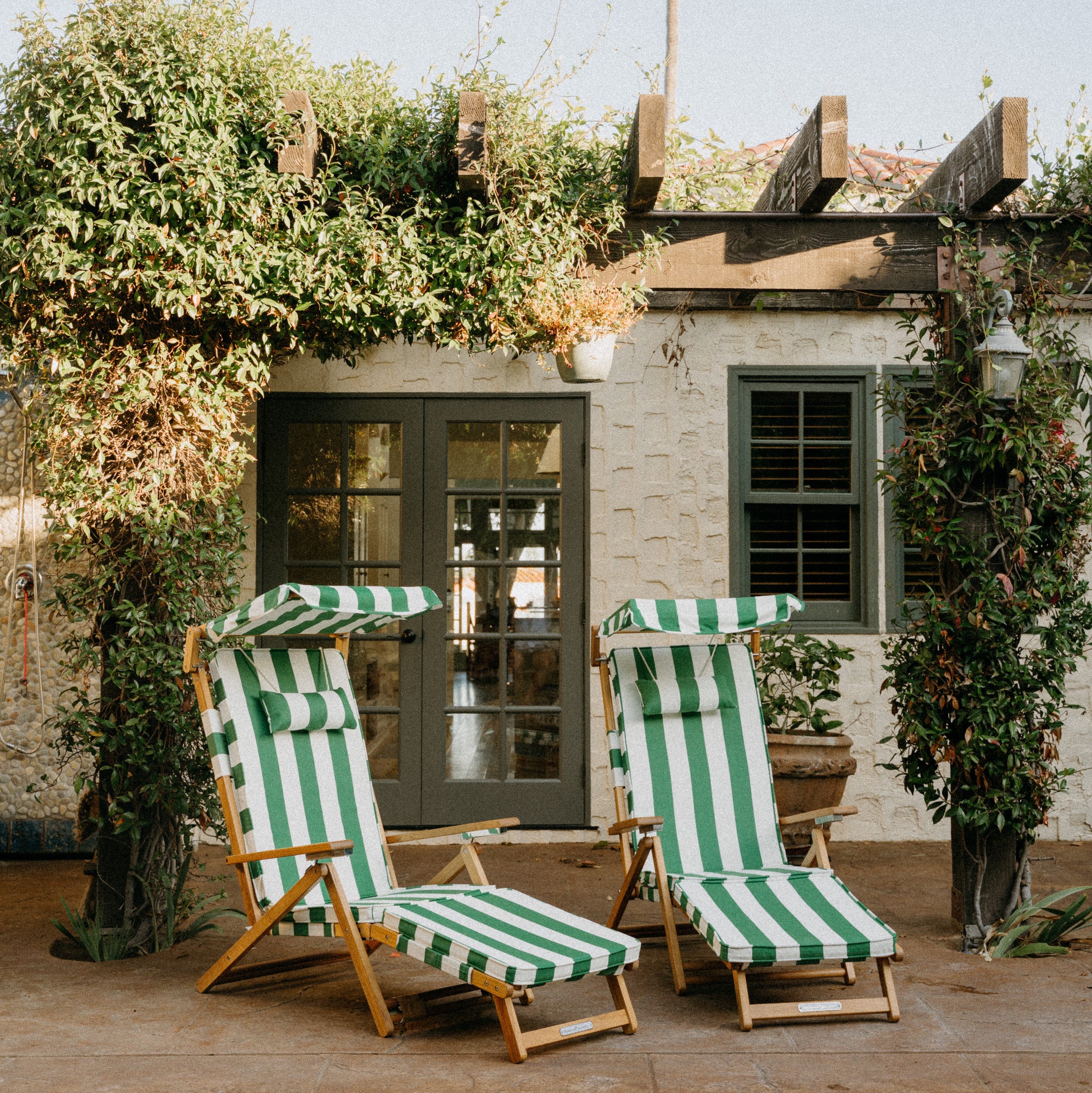 Two green and white striped lounge chairs by a pool with a palm tree in the background.