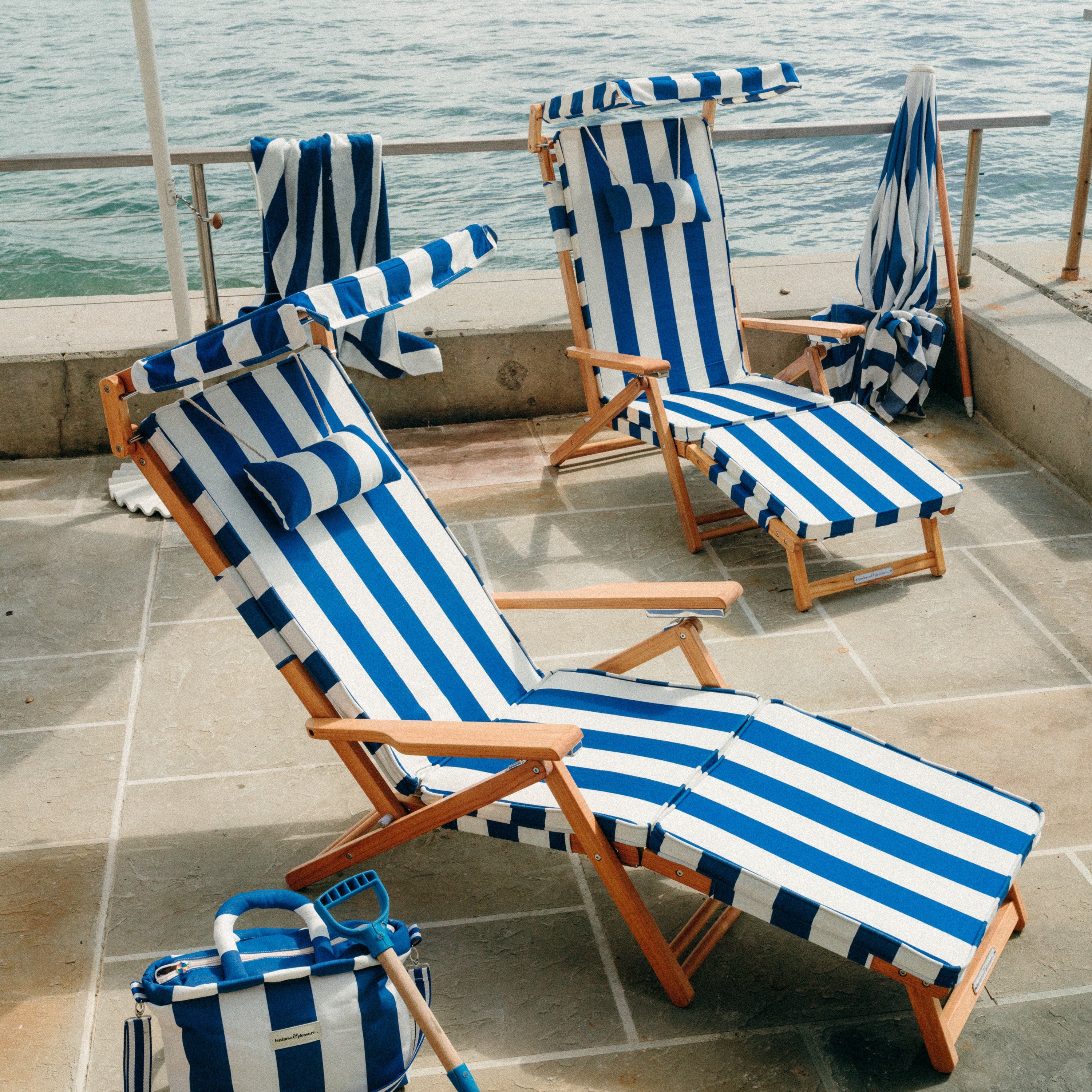 Blue and white striped beach chairs and bag on a tiled floor with ocean view.