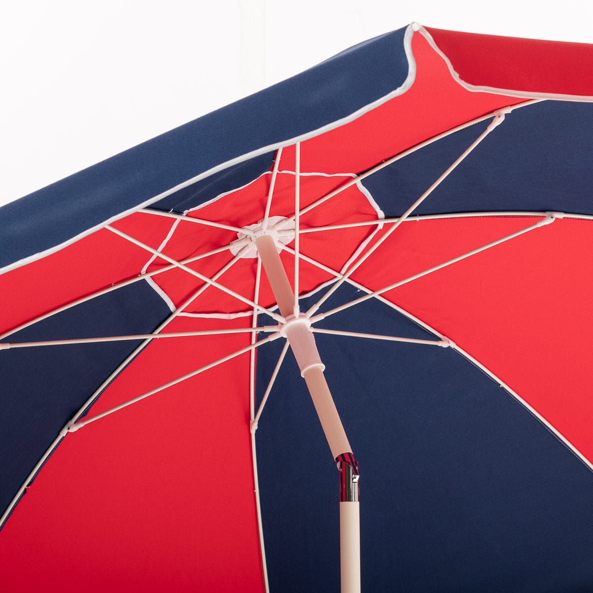 Red and navy beach umbrella with hinged pole detail on a white background