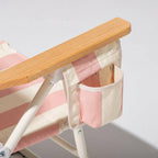 Foldable chair with pink and white striped seat and wooden armrests with drink holder on a light gray background