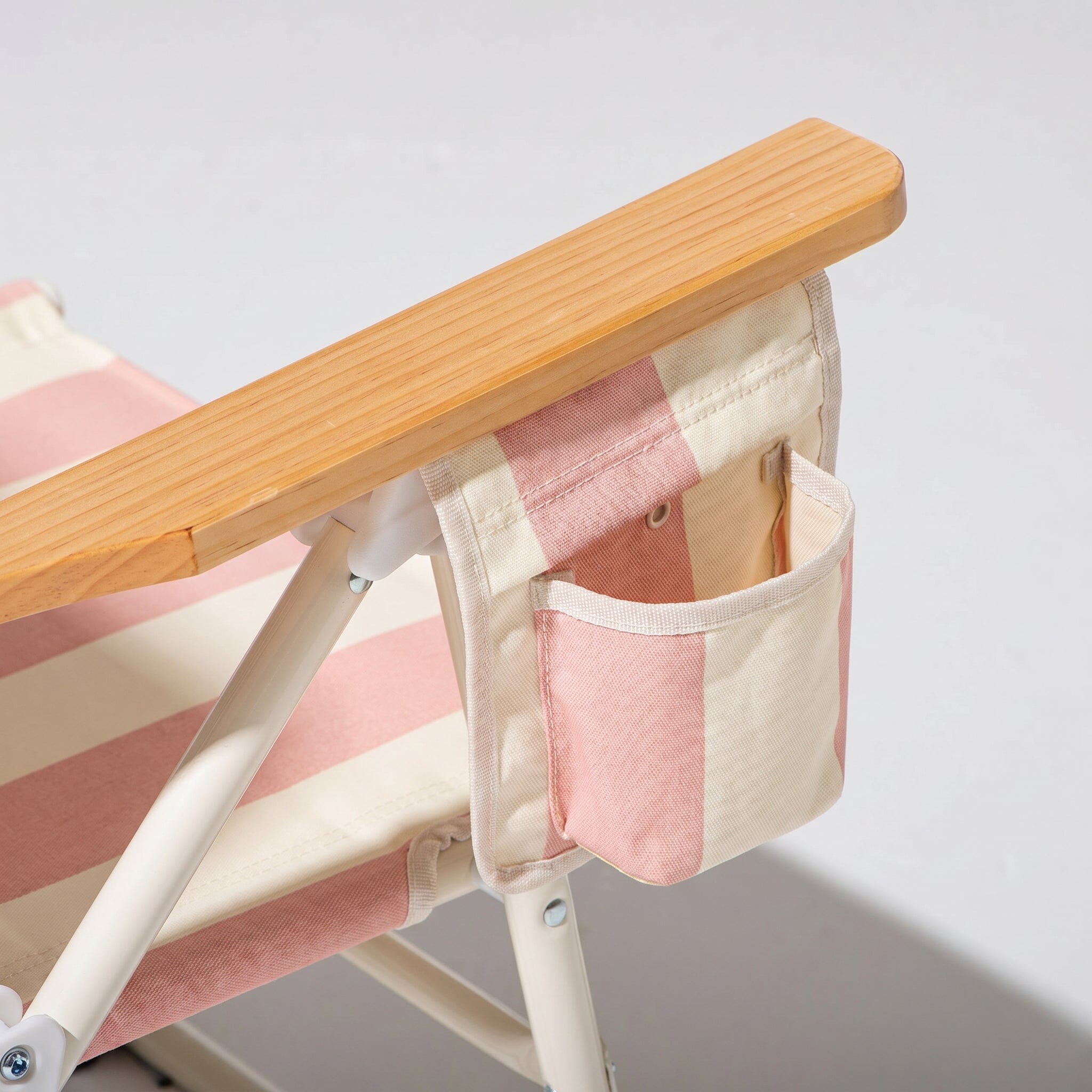 Foldable chair with pink and white striped seat and wooden armrests with drink holder on a light gray background