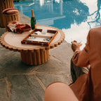 Person sitting by a poolside with a backgammon set and bottle of wine on a small table.