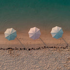Three beach umbrellas with a blue and white polka dot pattern are lined up on a sandy beach under a turquoise ocean.