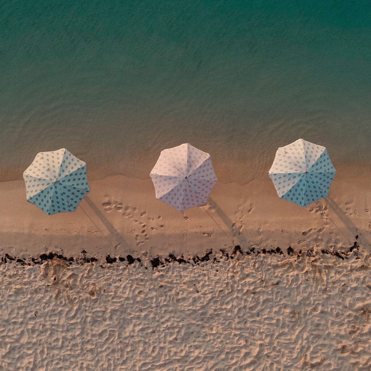 Three beach umbrellas with a blue and white polka dot pattern are lined up on a sandy beach under a turquoise ocean.