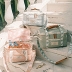 Three insulated tote bags arranged on white stone steps outdoors. One pale pink bag in the foreground is open and filled with bottles, one pale mint green bag sits to the right, and one very light icy blue bag is positioned higher in the background.