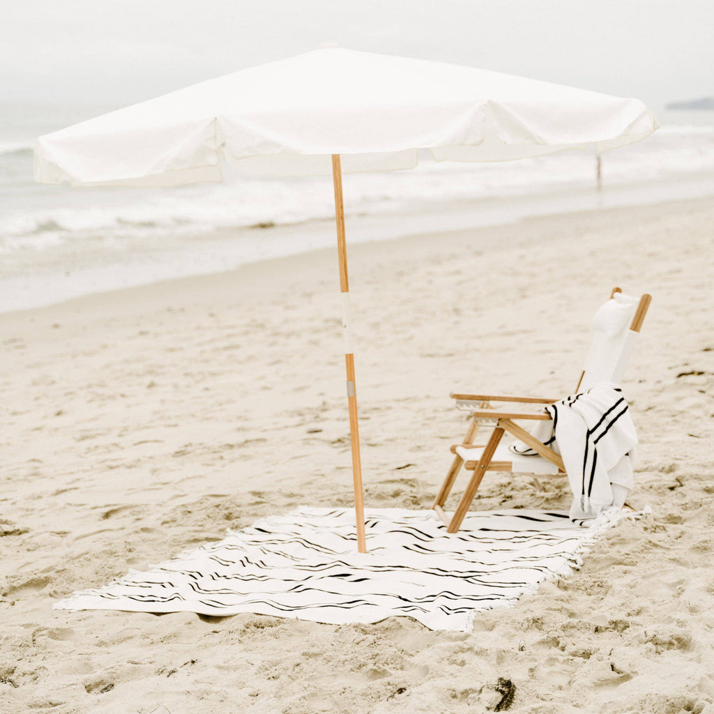 white amalfi umbrella at the beach with chair and blanket