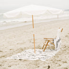 white amalfi umbrella at the beach with chair and blanket