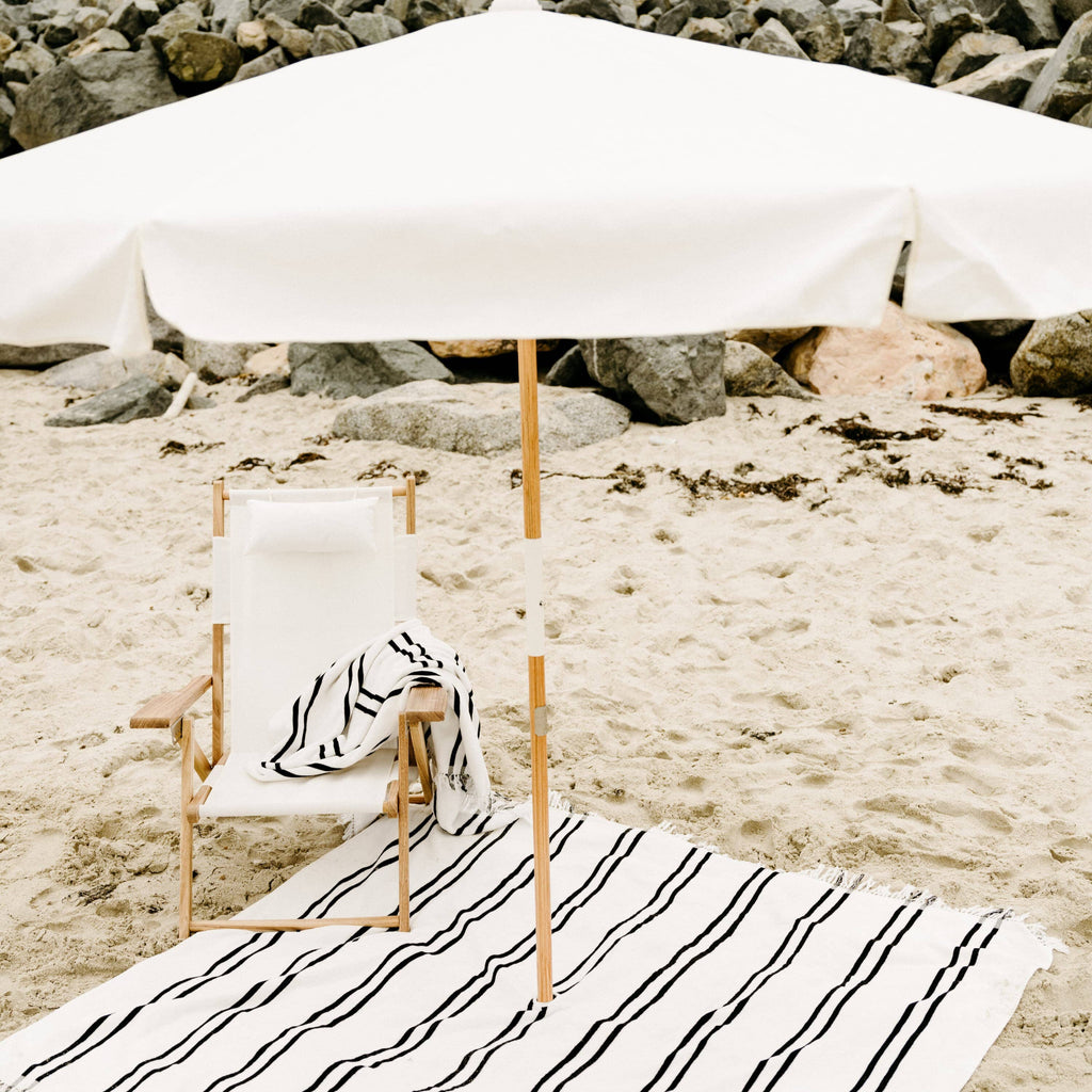 white amalfi umbrella at the beach with chair and blanket