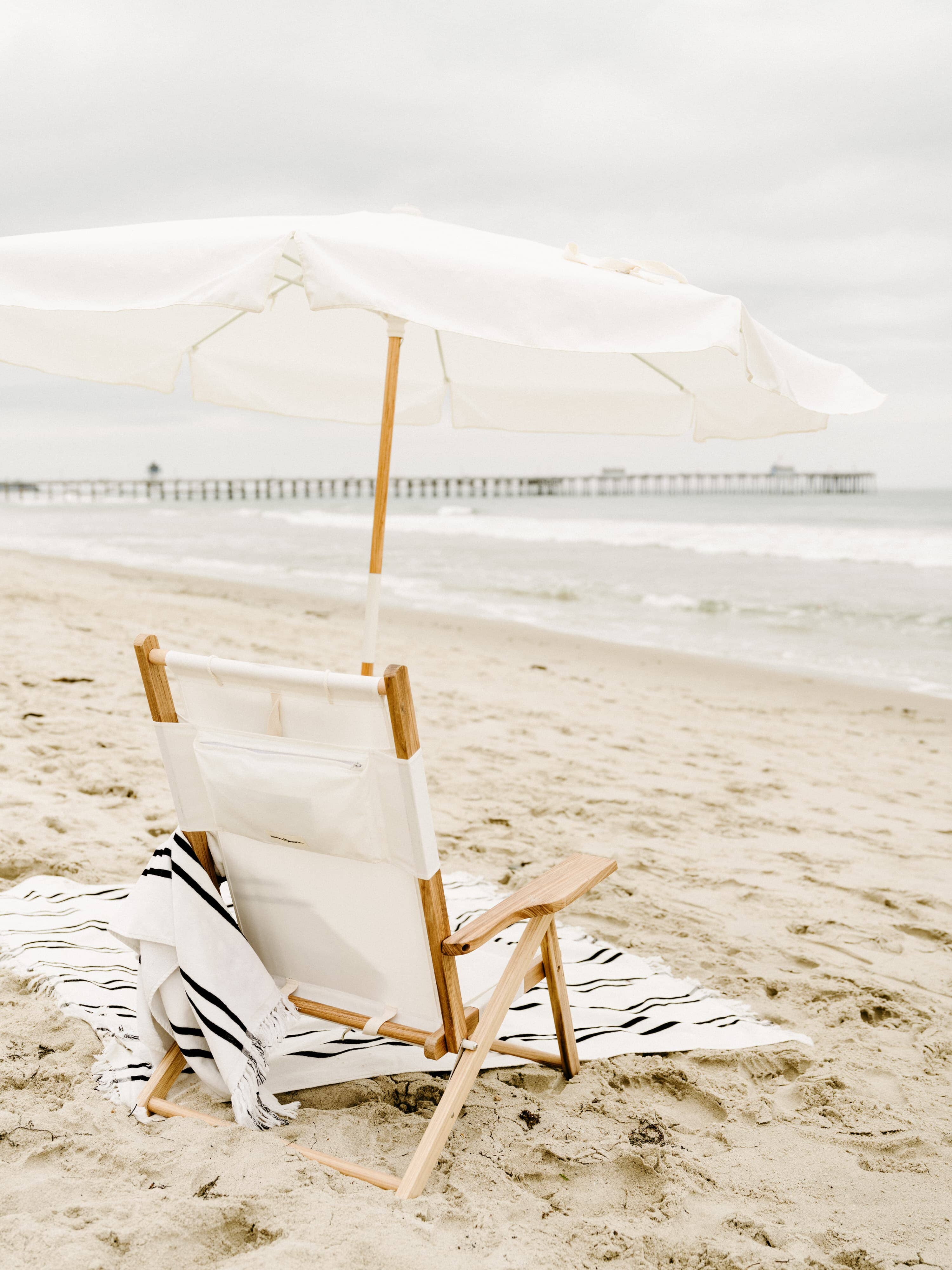 white amalfi umbrella at the beach with chair and blanket