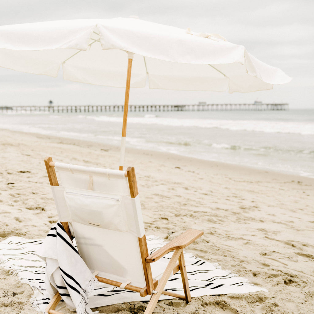 white amalfi umbrella at the beach with chair and blanket