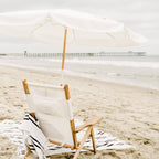 white amalfi umbrella at the beach with chair and blanket