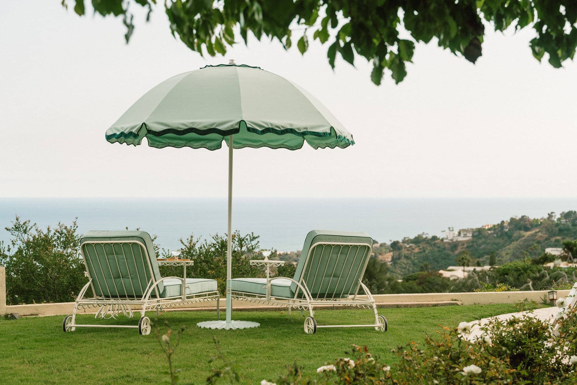 green patio umbrella and two sun loungers over looking the coastline