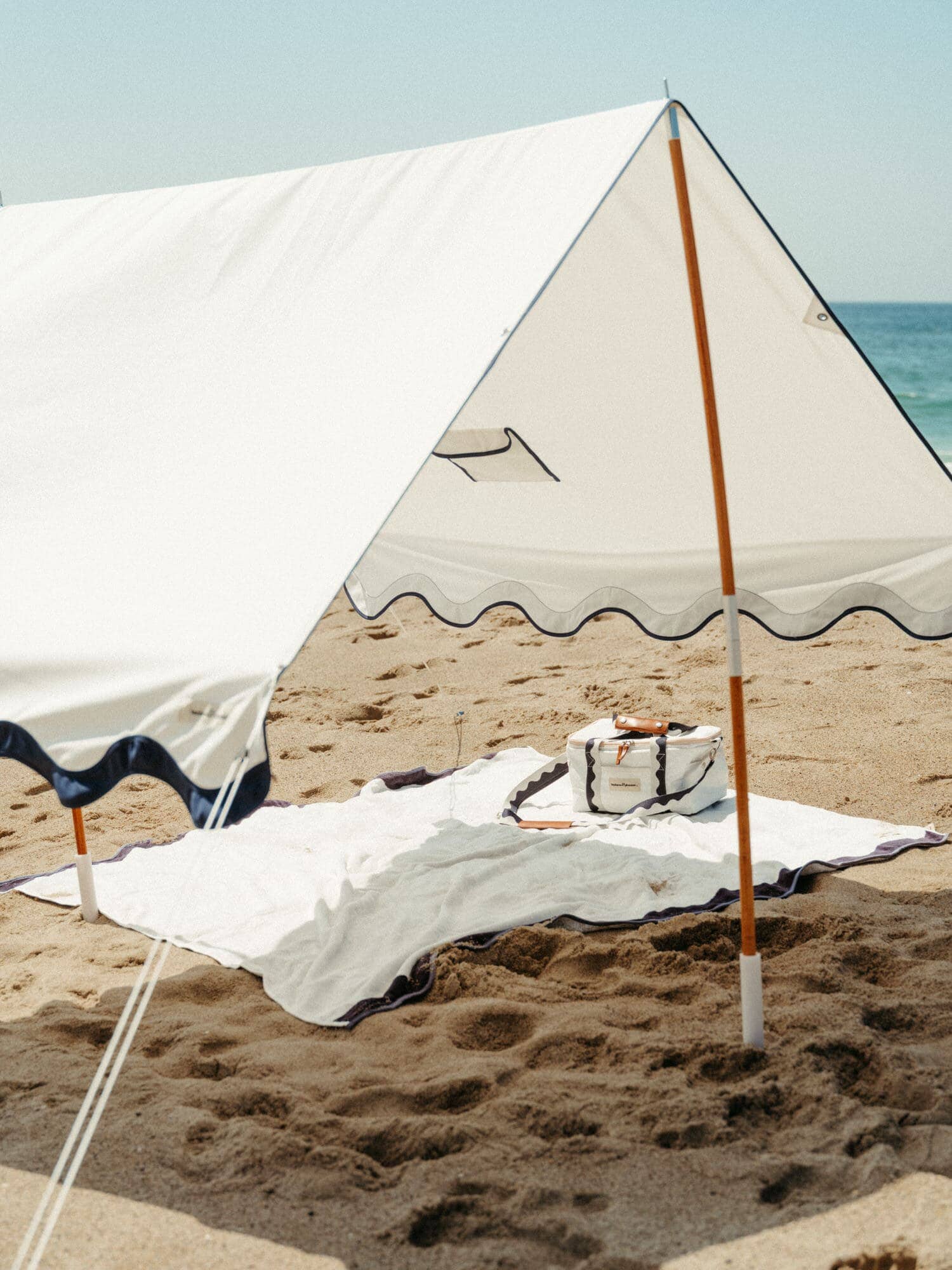 white riviera blanket, tent and cooler on a beach